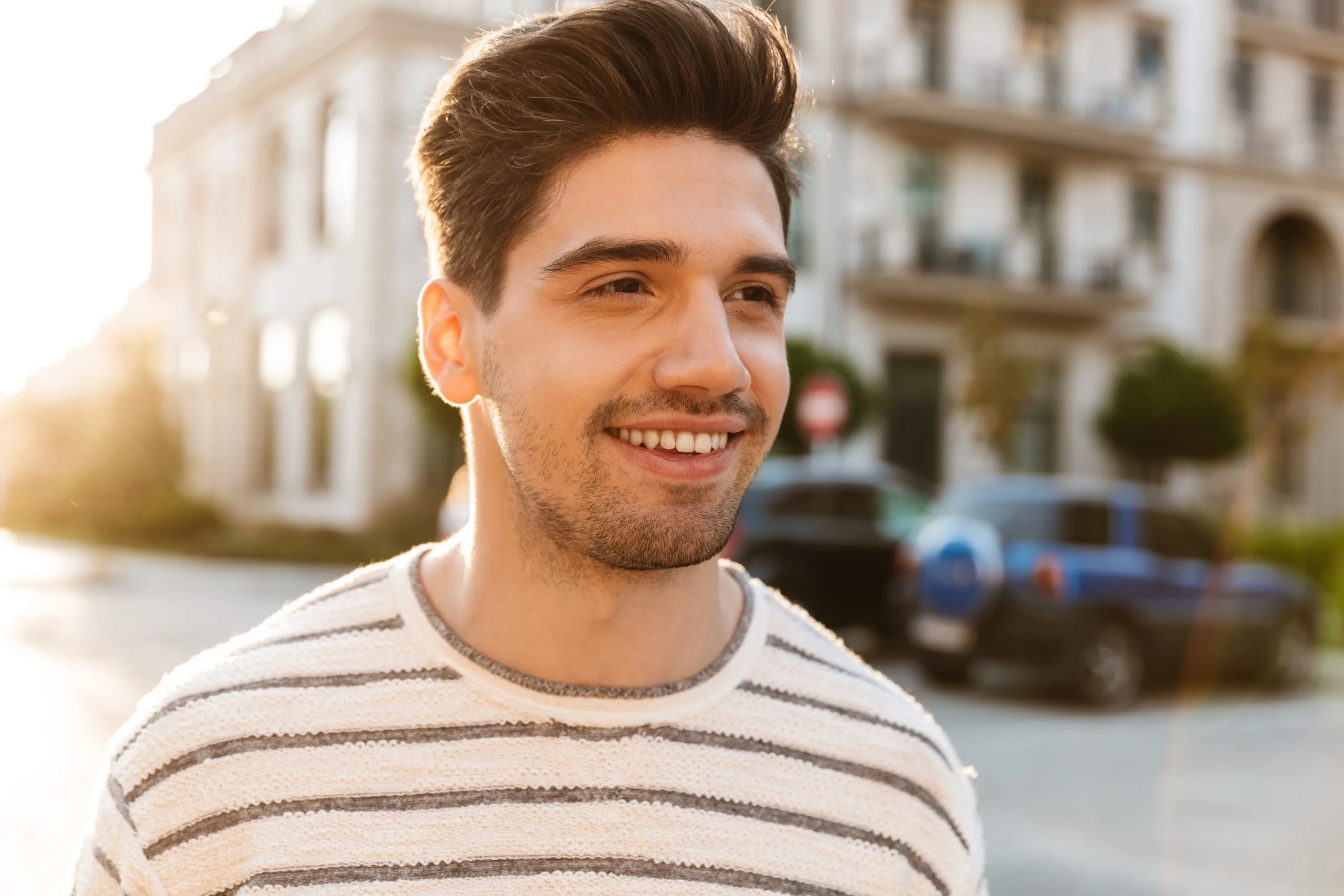 Young man smiling outdoors wearing striped shirt with residential building in background
