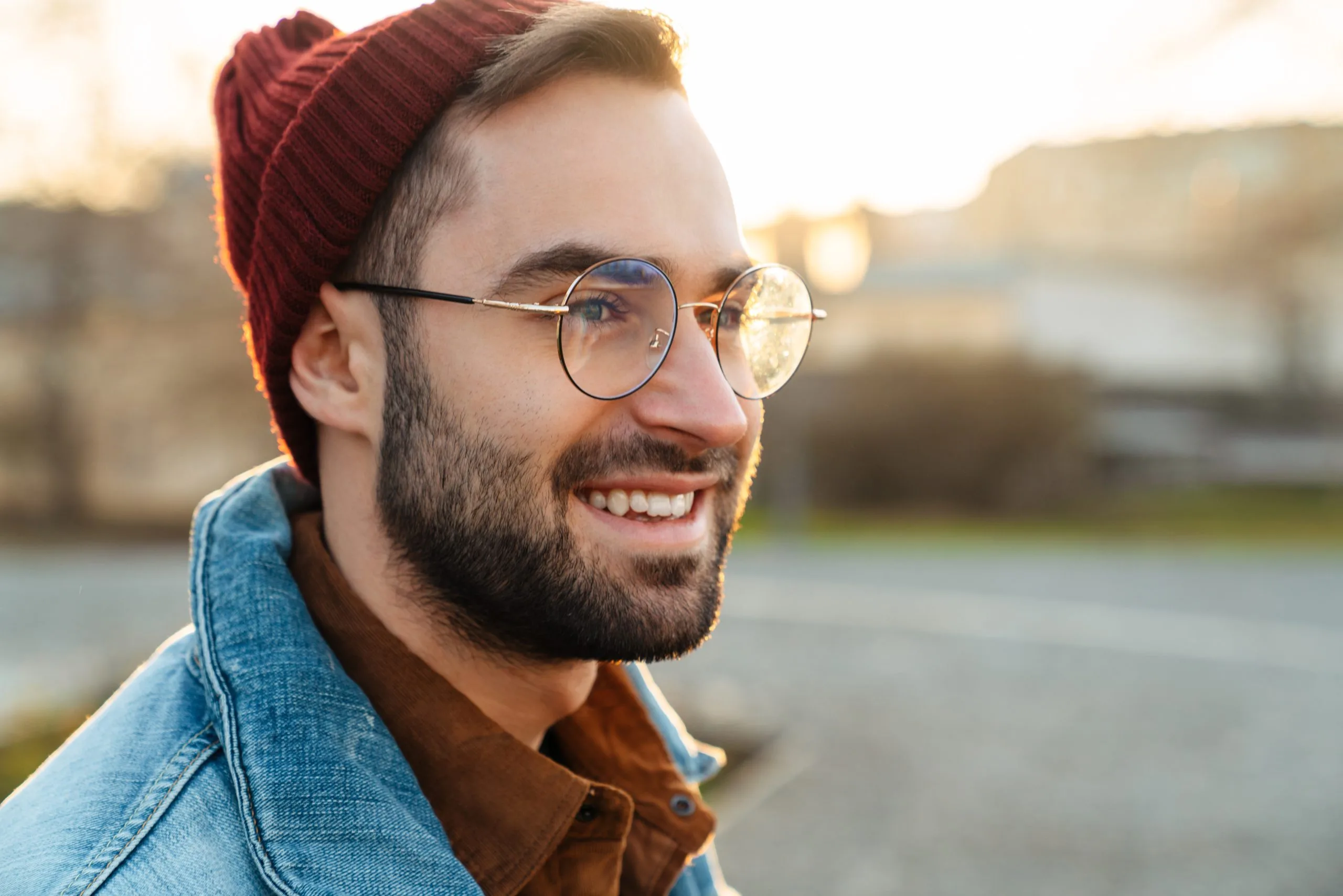 Smiling man wearing glasses and red beanie outdoors by water