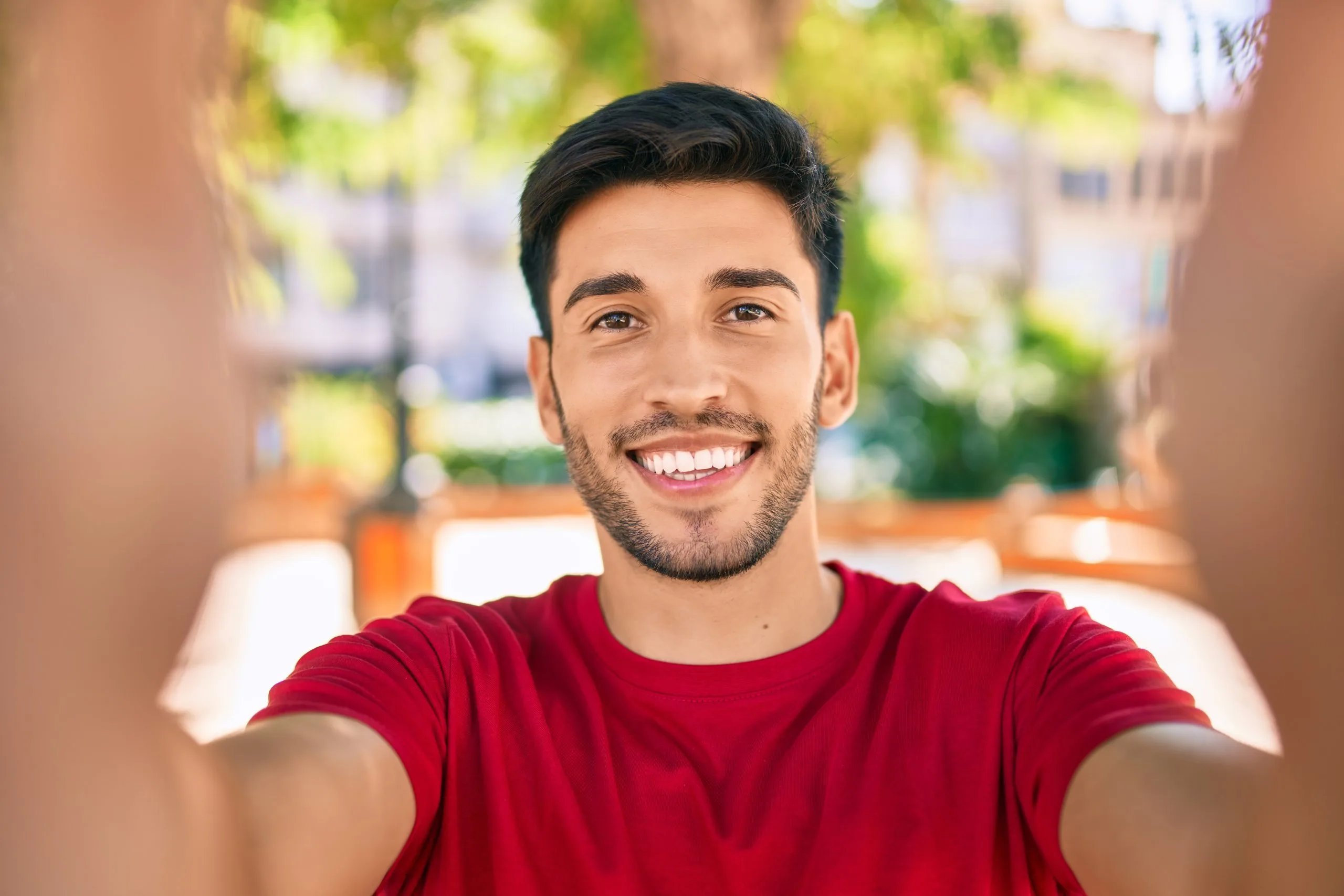 Smiling man in red shirt taking selfie in urban setting