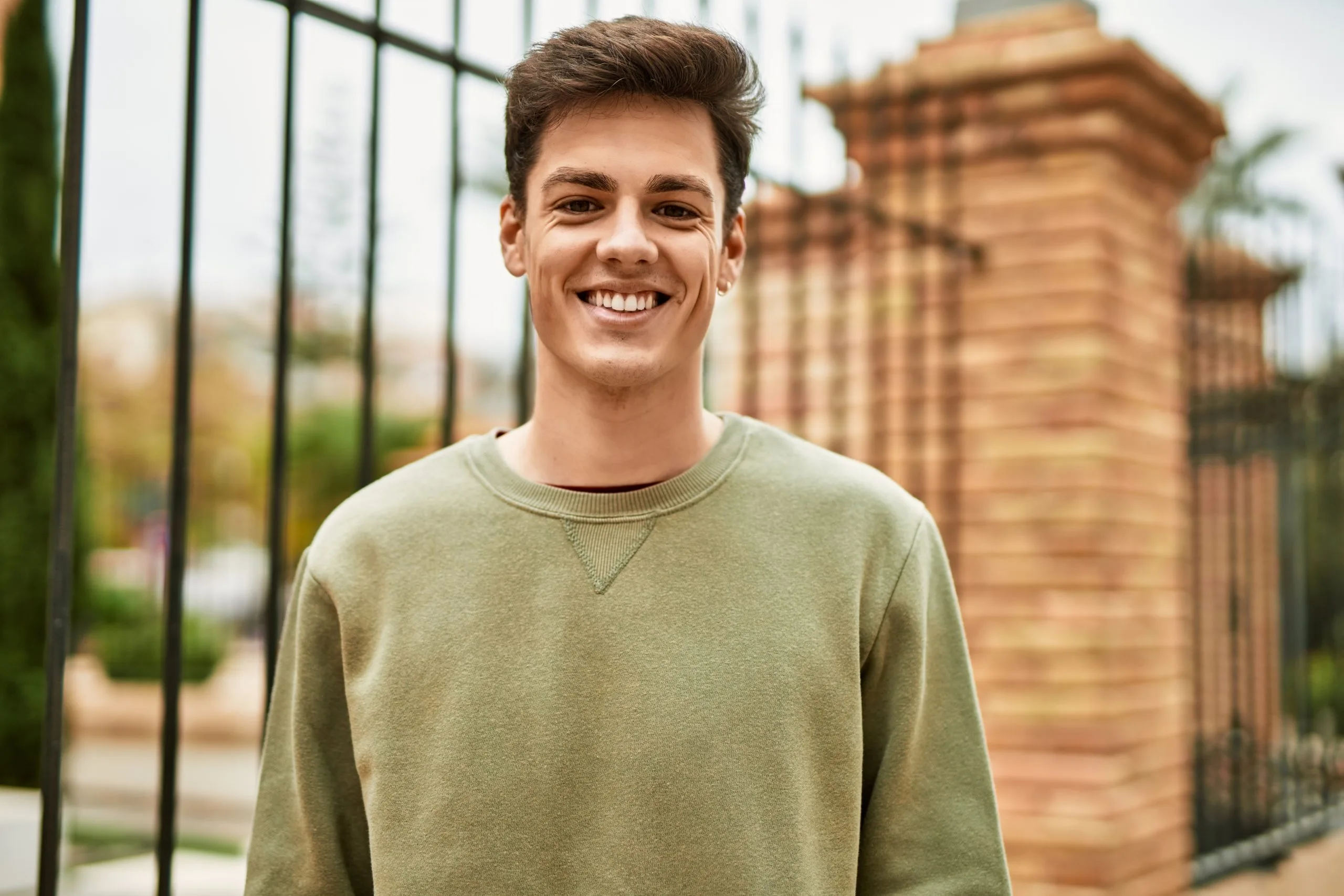 Smiling man in olive sweatshirt standing outdoors in front of a brick building
