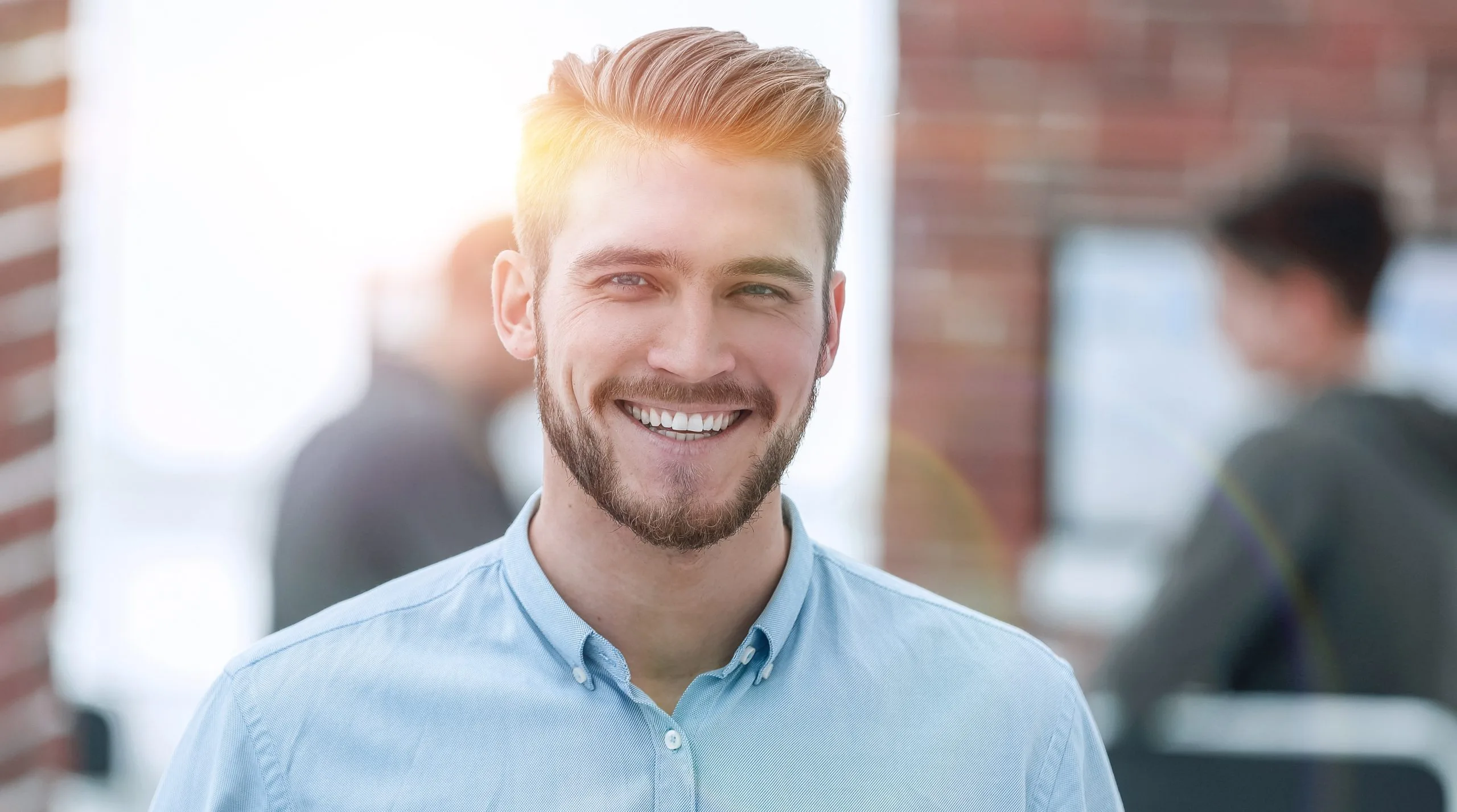 Smiling man with reddish-blonde hair wearing light blue shirt in office setting