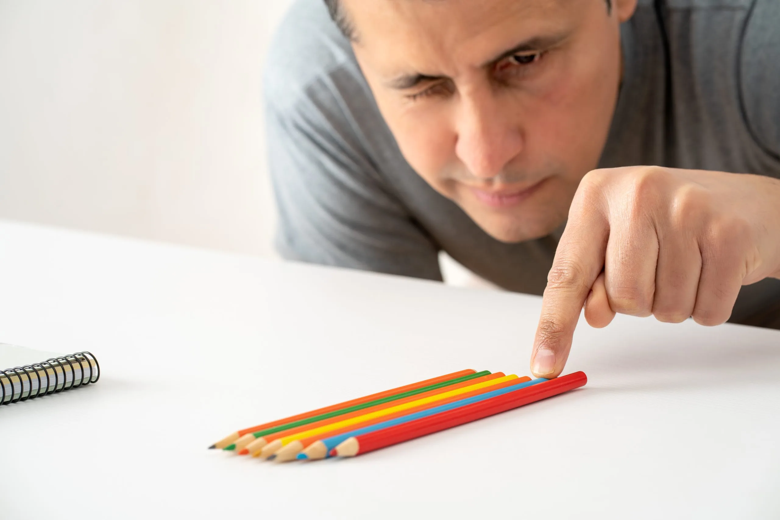 Person selecting a red colored pencil from a row of sharpened pencils on desk