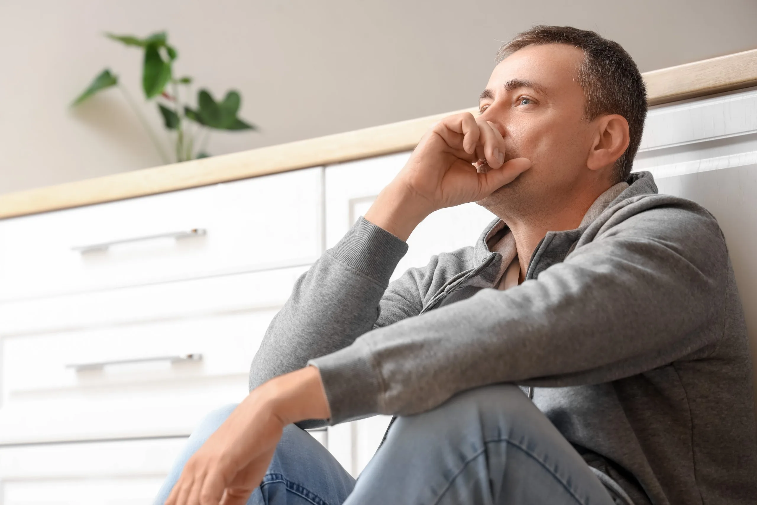 Man sitting against white cabinets with hand to face, displaying anxious expression
