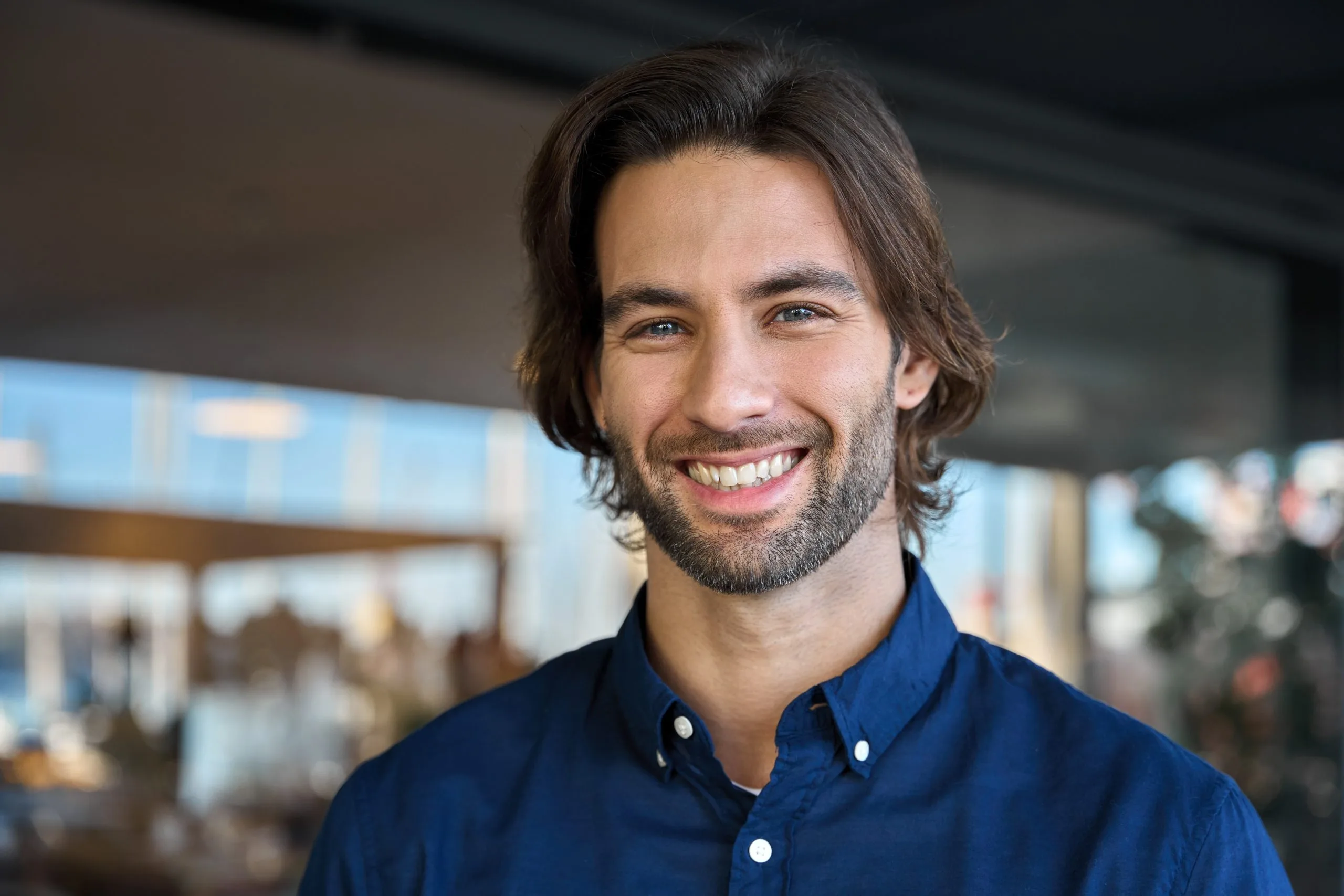 Man with long dark hair smiling in modern interior space with city view