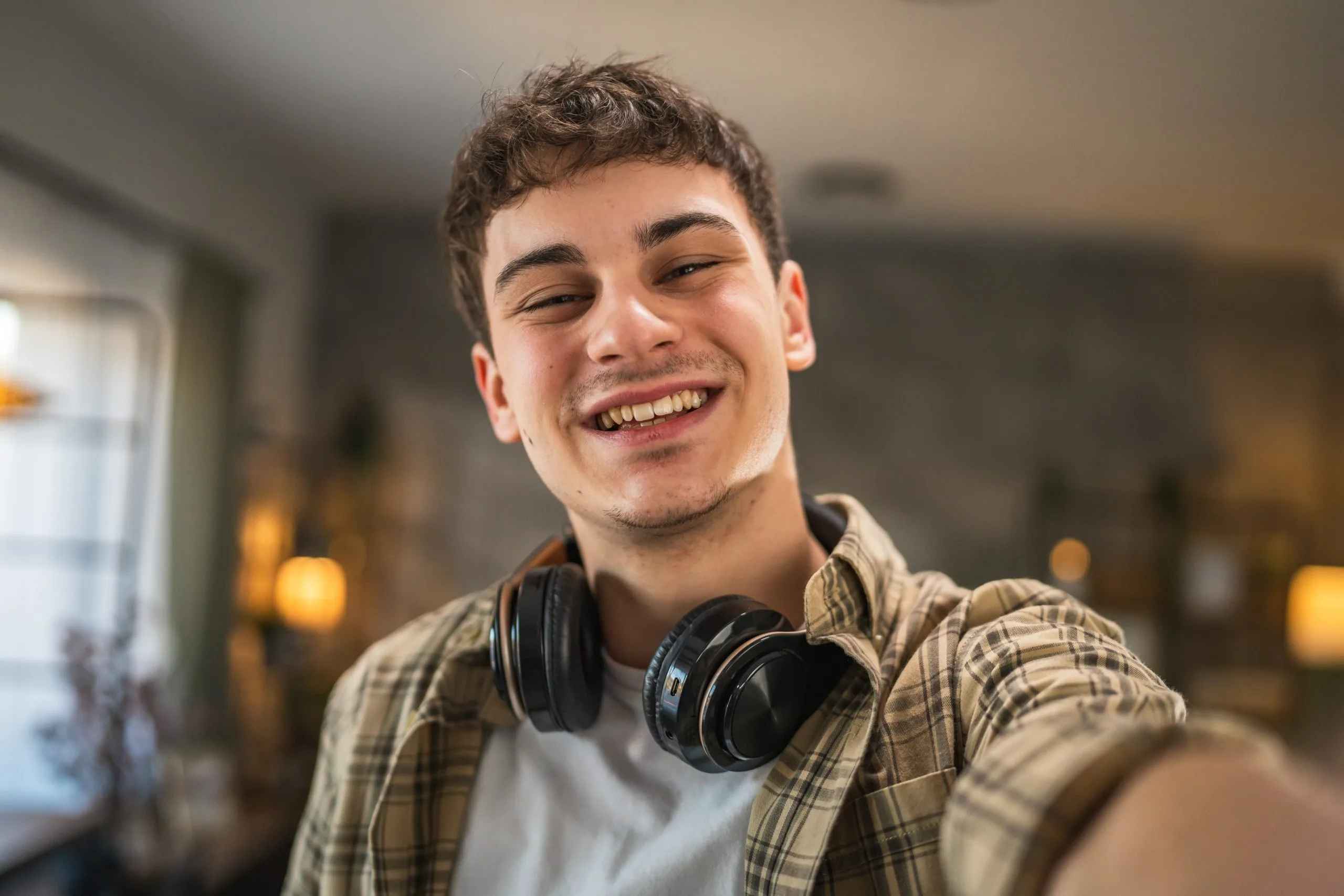 Smiling young man wearing black headphones around neck and plaid shirt