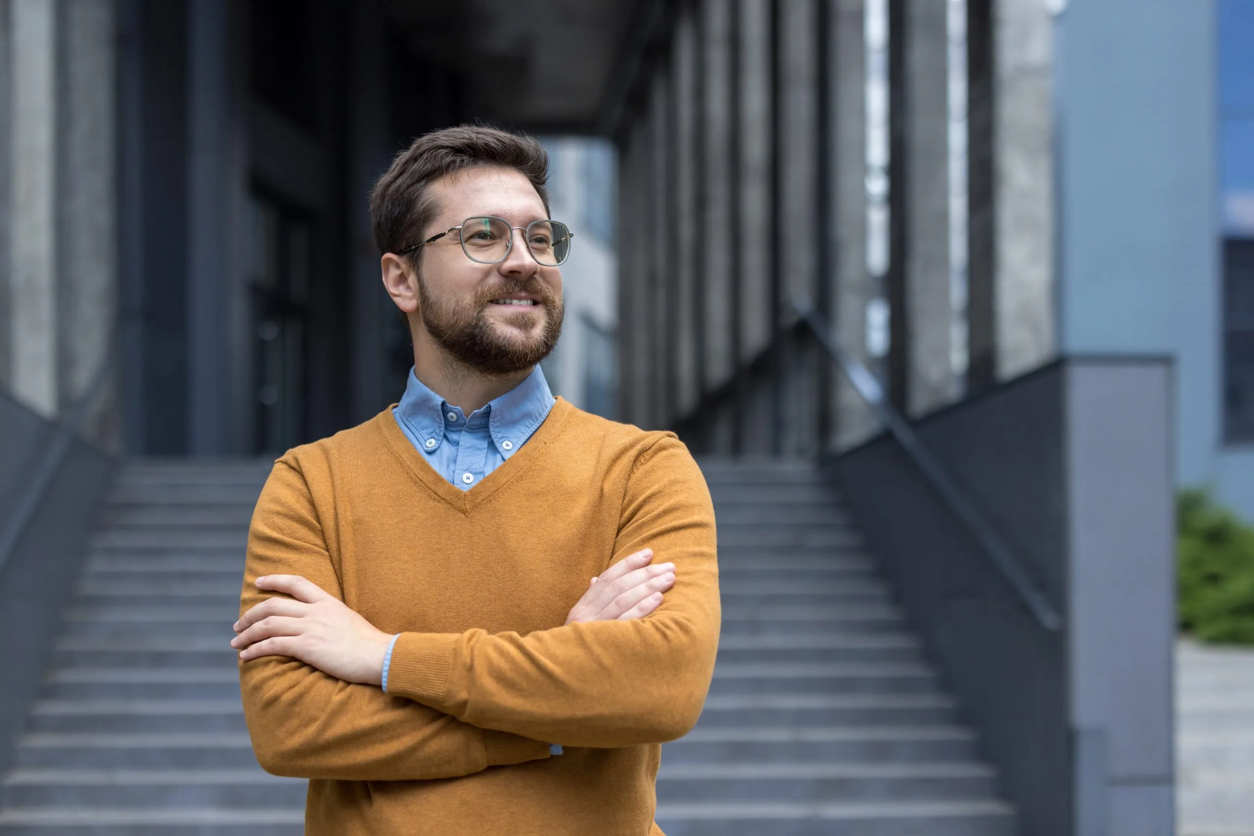 Man with glasses and crossed arms standing in modern urban corridor
