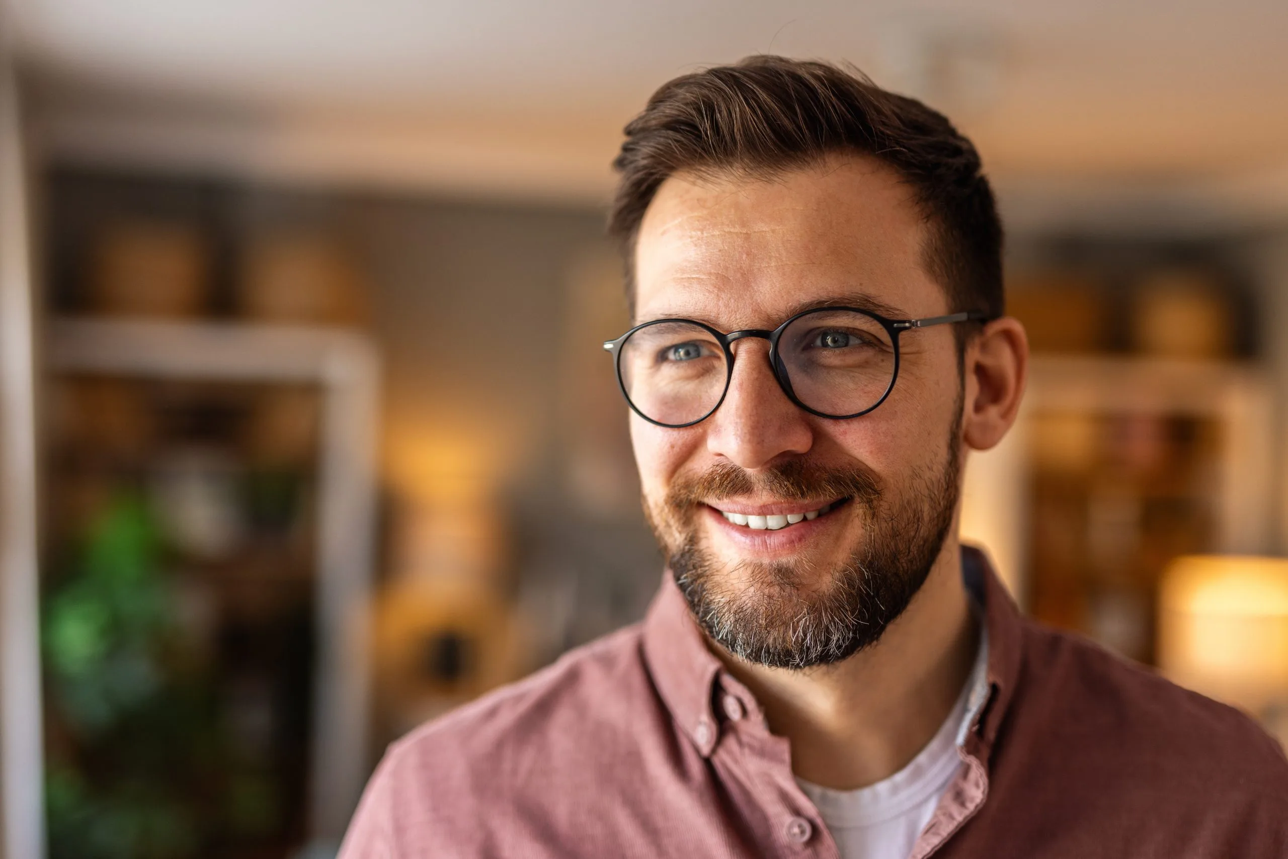 Smiling man wearing glasses and pink button-up shirt in warm-lit interior