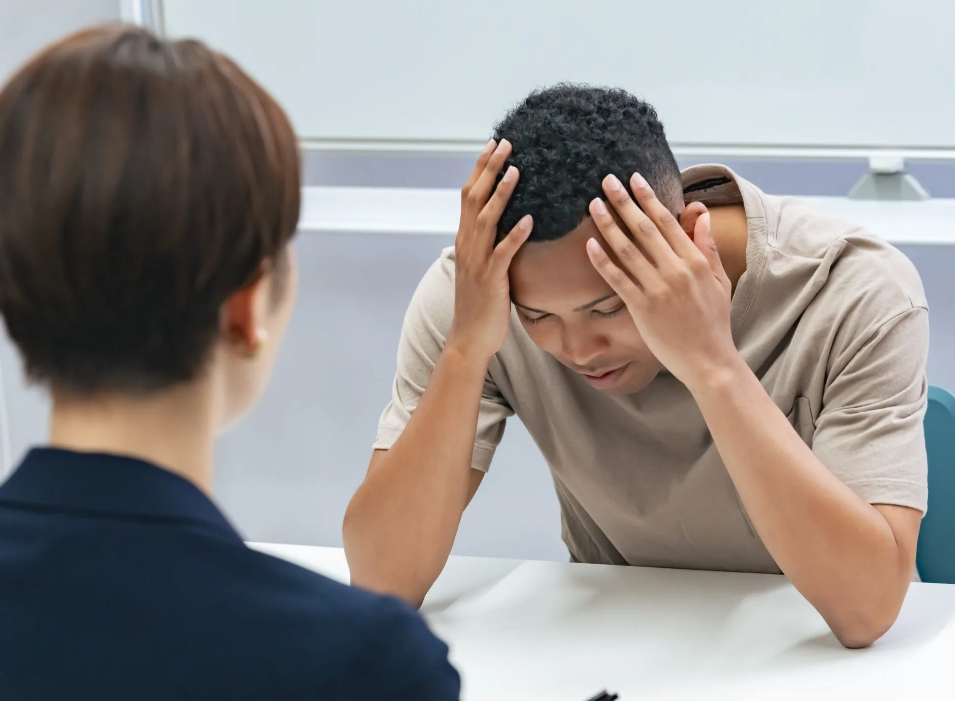 Man with hands on head appearing distressed while speaking with healthcare provider across table