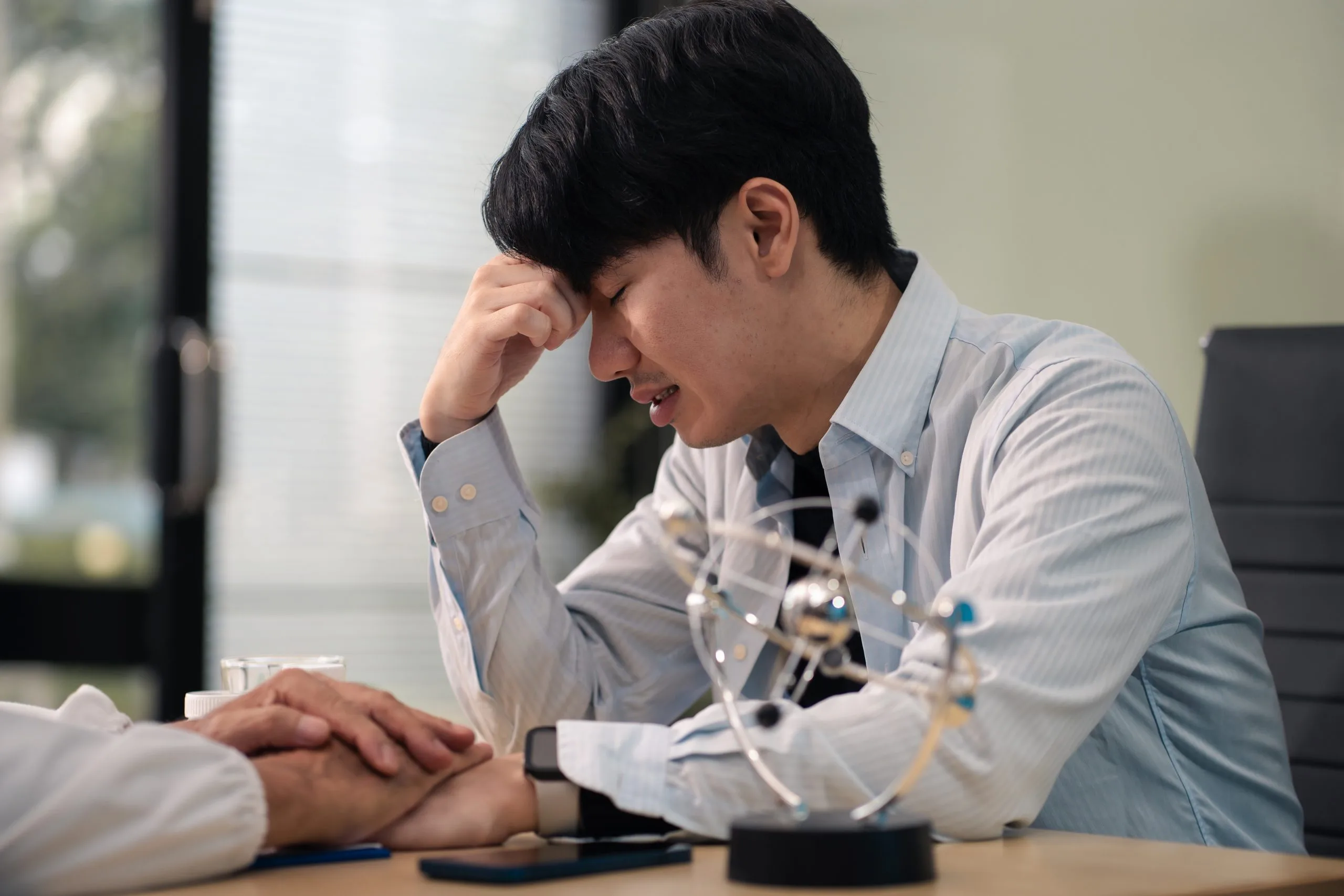 Man with hand to head appearing stressed during professional discussion at desk
