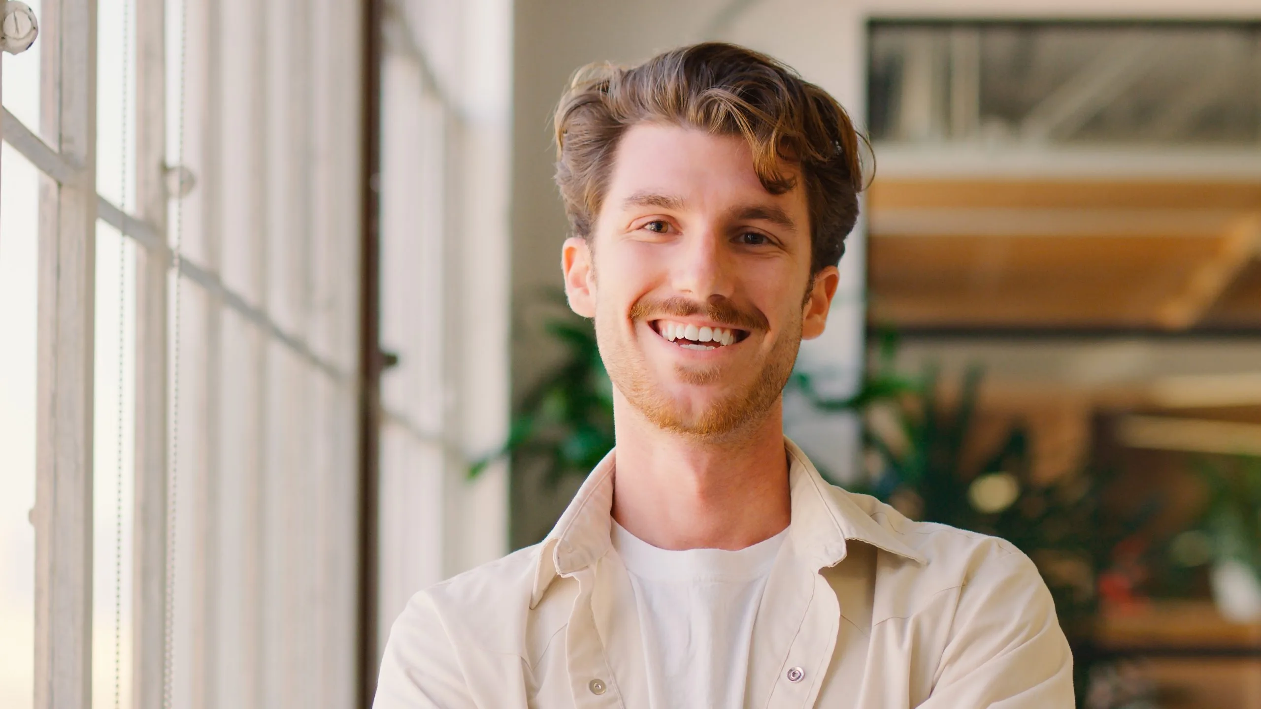 Smiling man in beige shirt standing by a bright window in a modern interior