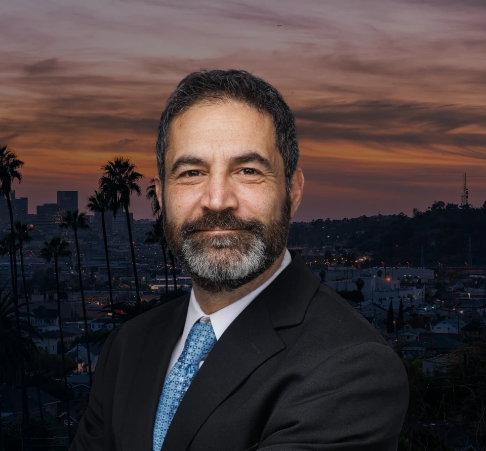 Professional man in dark suit and blue tie against sunset cityscape with palm trees