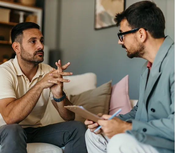 Man in therapy session talking with a clinician taking notes