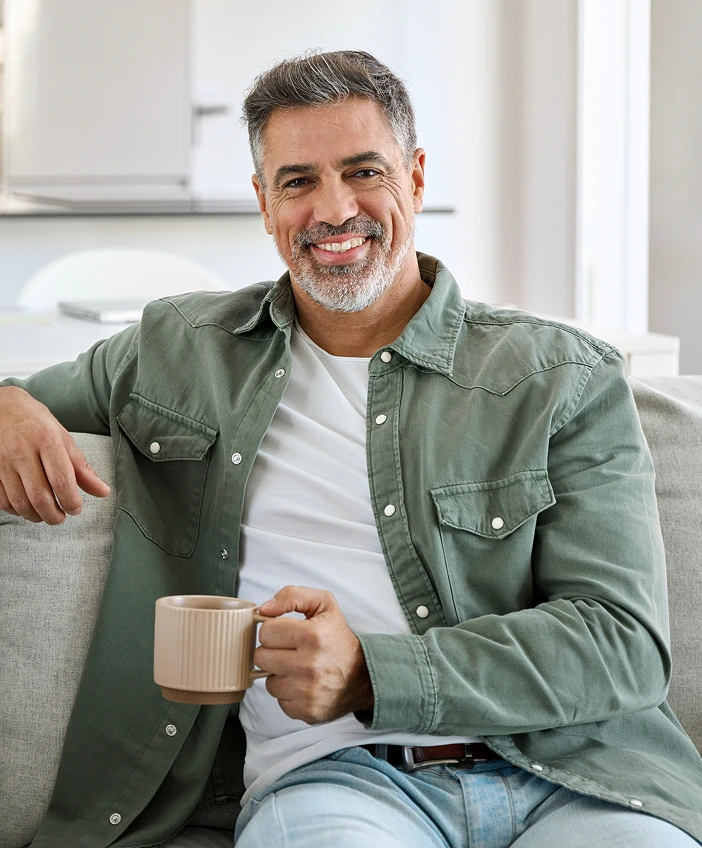 Man in a sage green shirt holding a beige mug, smiling in a modern clinical setting