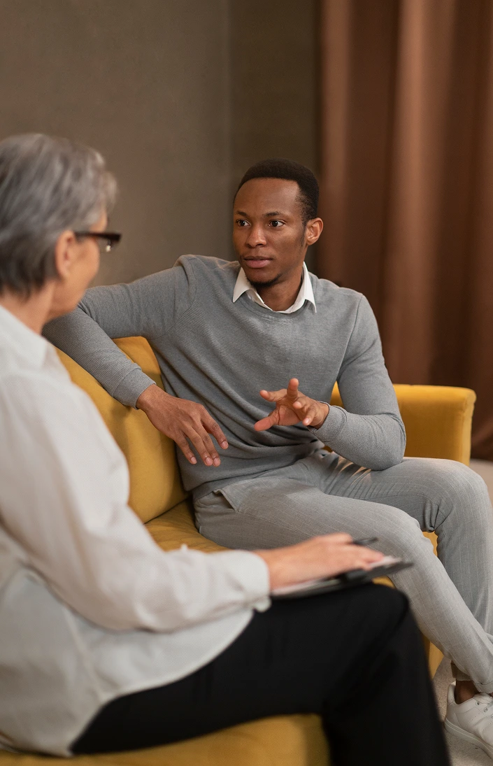 Older woman with glasses listening to a young man in a yellow chair during a therapy session