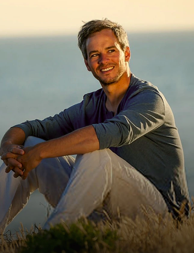 Man smiling at sunset overlooking ocean while sitting outdoors