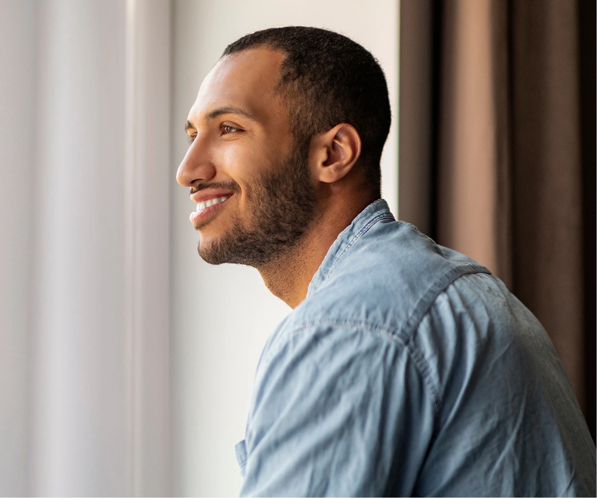 Smiling man in light blue shirt looking toward window with natural sunlight