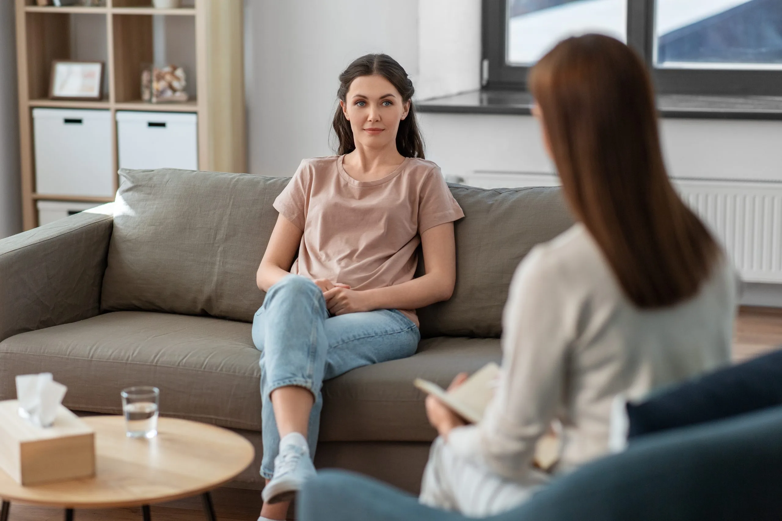 Therapist and client in session on couch, client speaking while therapist takes notes