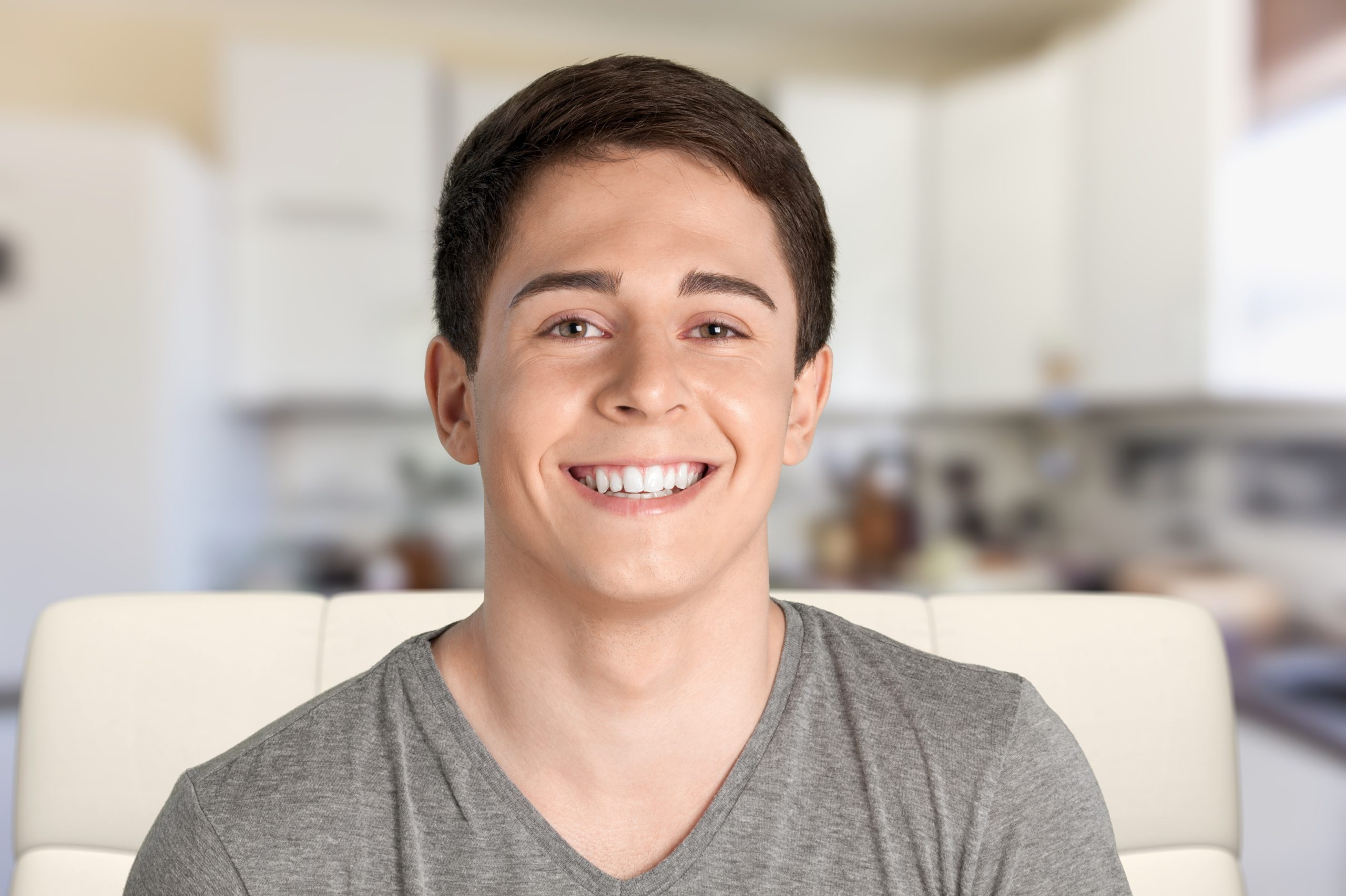 Young man smiling at camera in casual gray shirt indoors