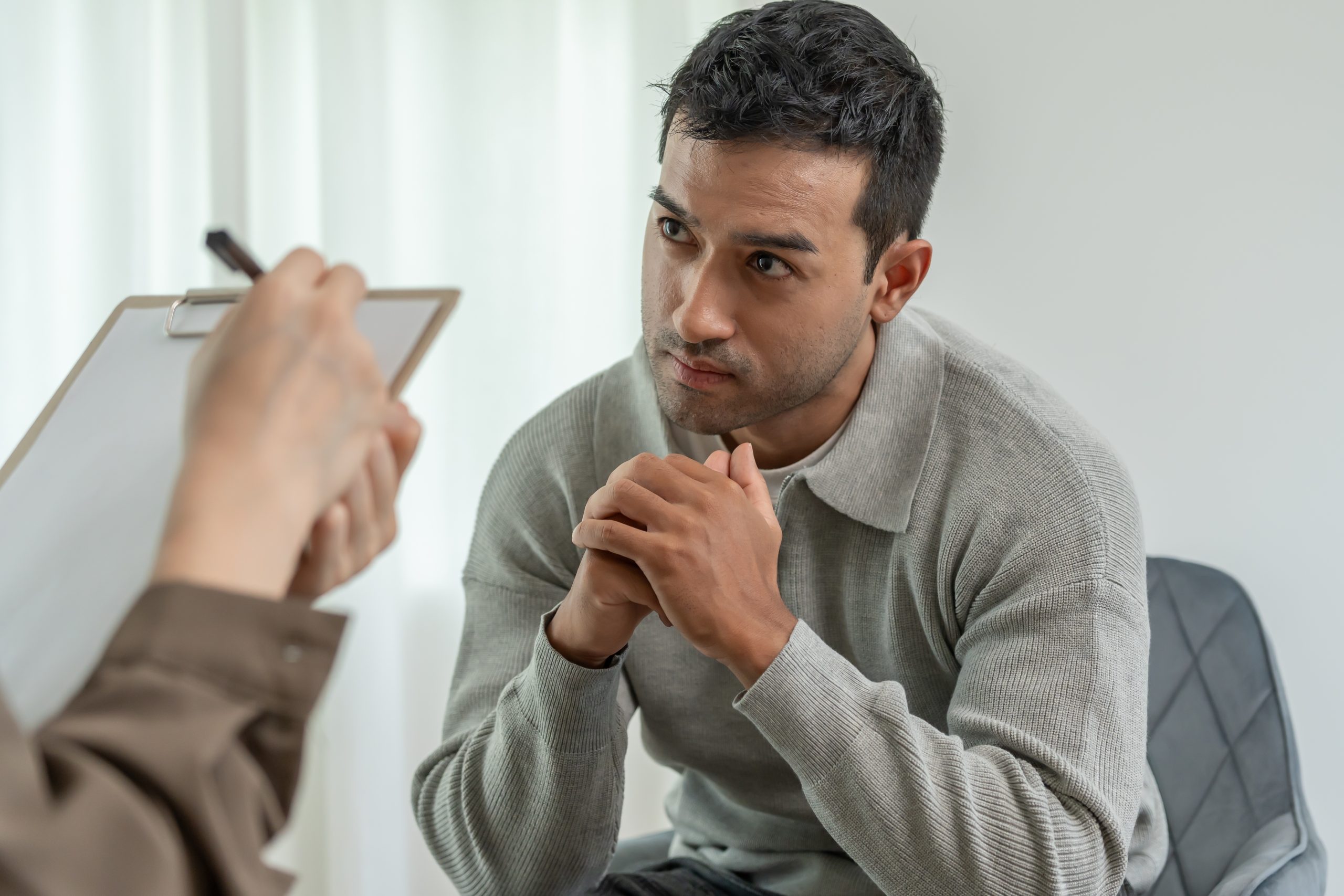 Man in gray shirt speaking with therapist holding clipboard