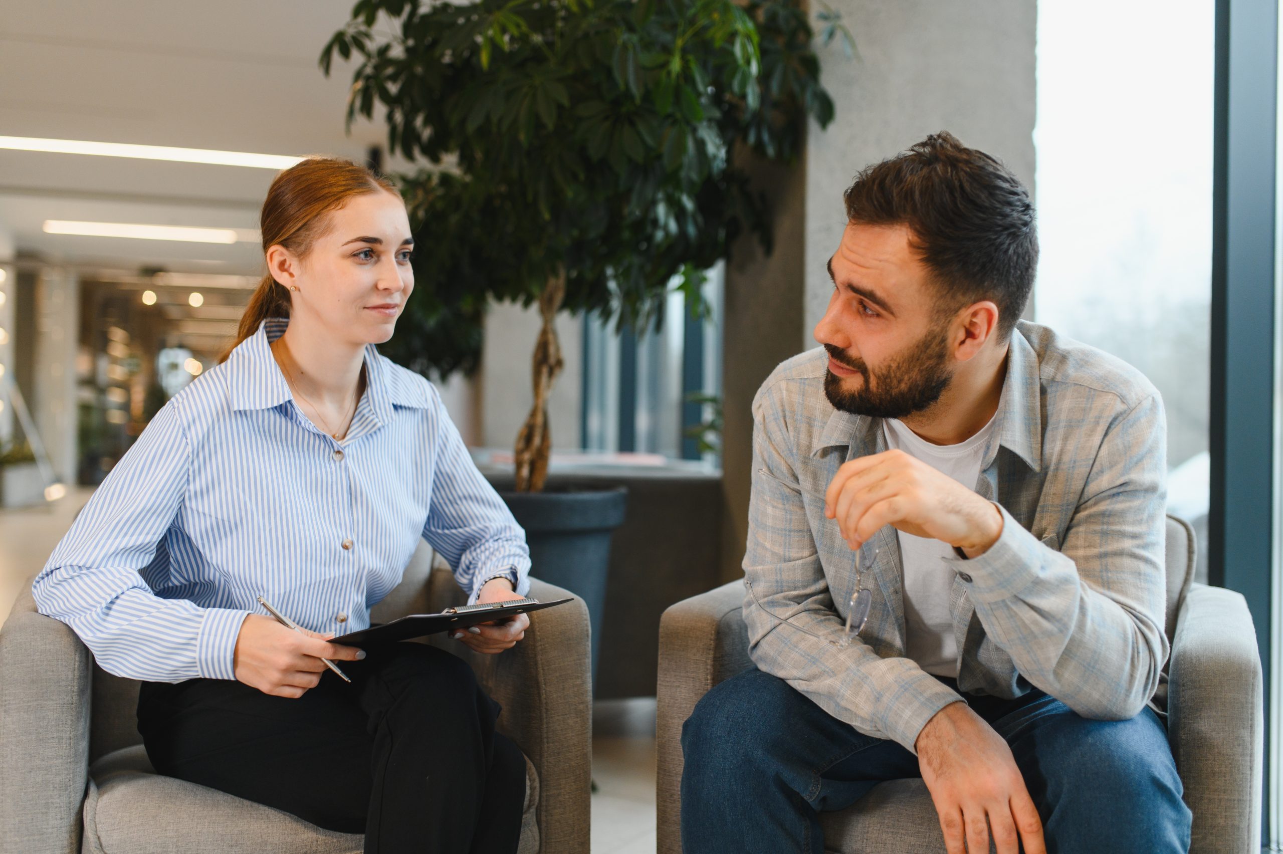 Therapist with clipboard listening to male client during counseling session