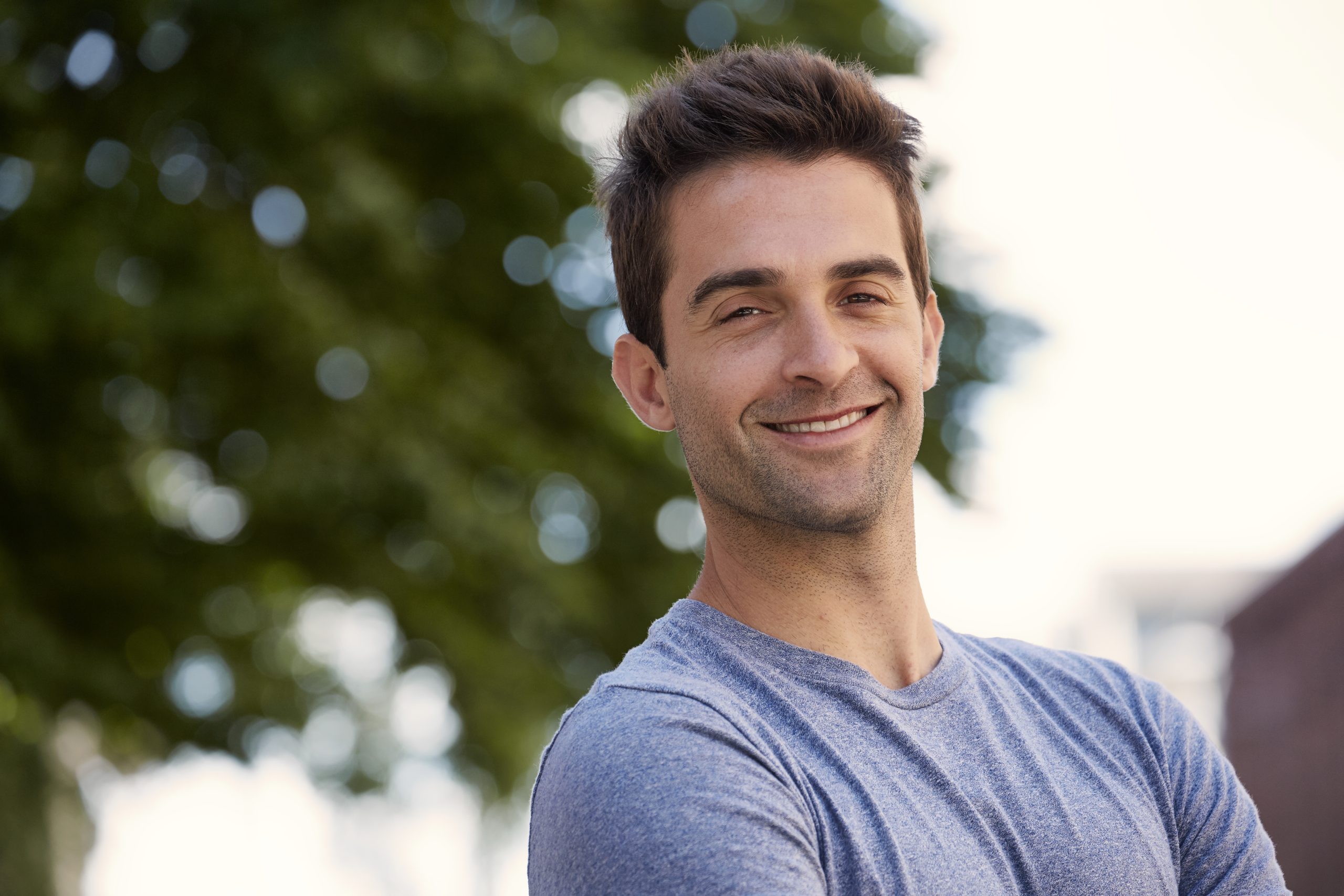 Man smiling outdoors with blurred green foliage in background