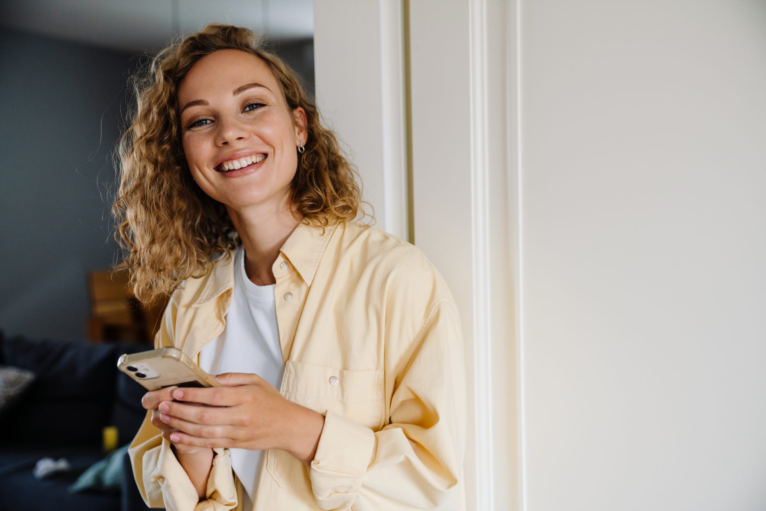 Woman in a beige shirt smiling while holding a phone in a modern interior