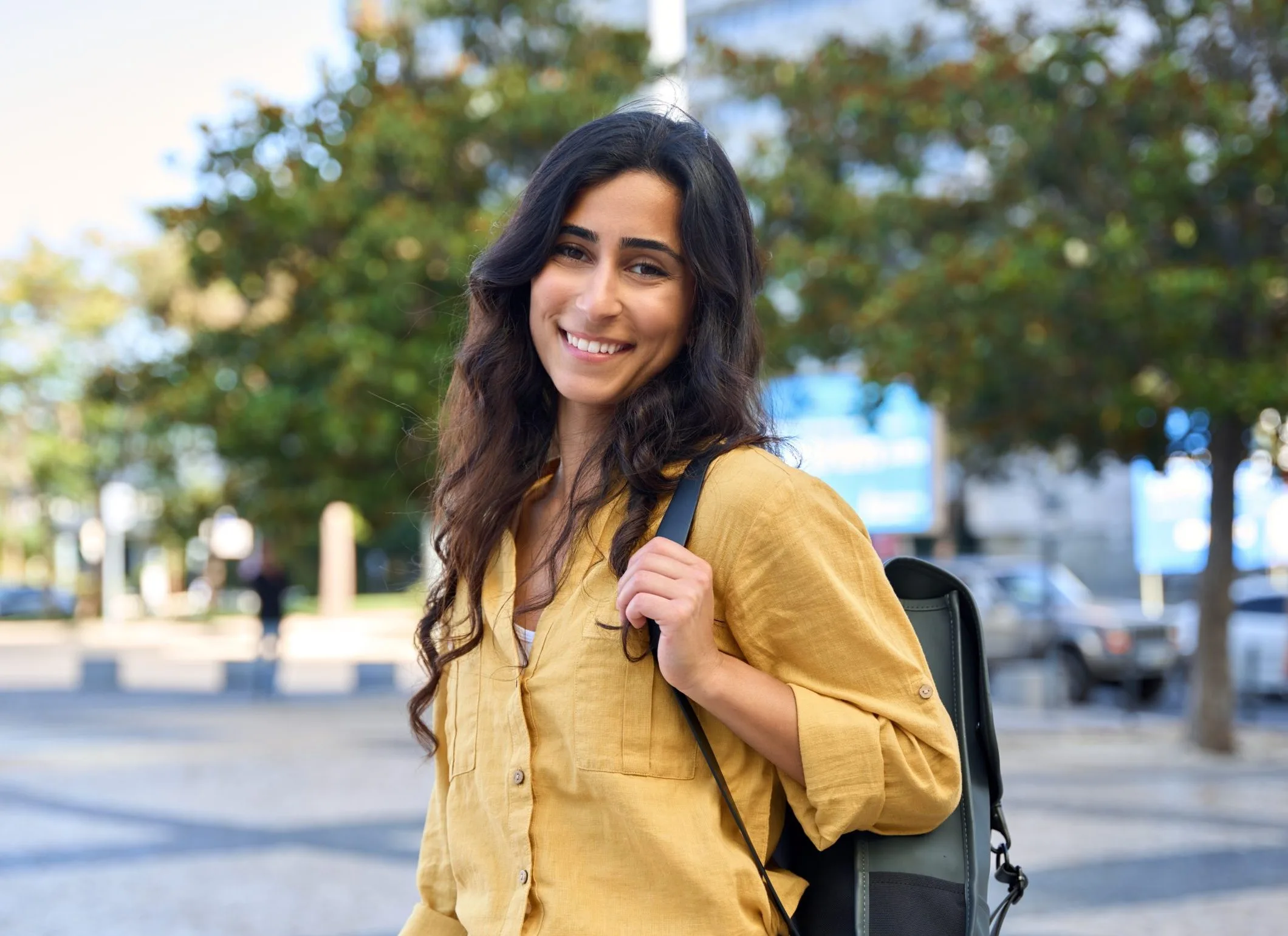 Smiling young woman wearing a yellow shirt and backpack outdoors