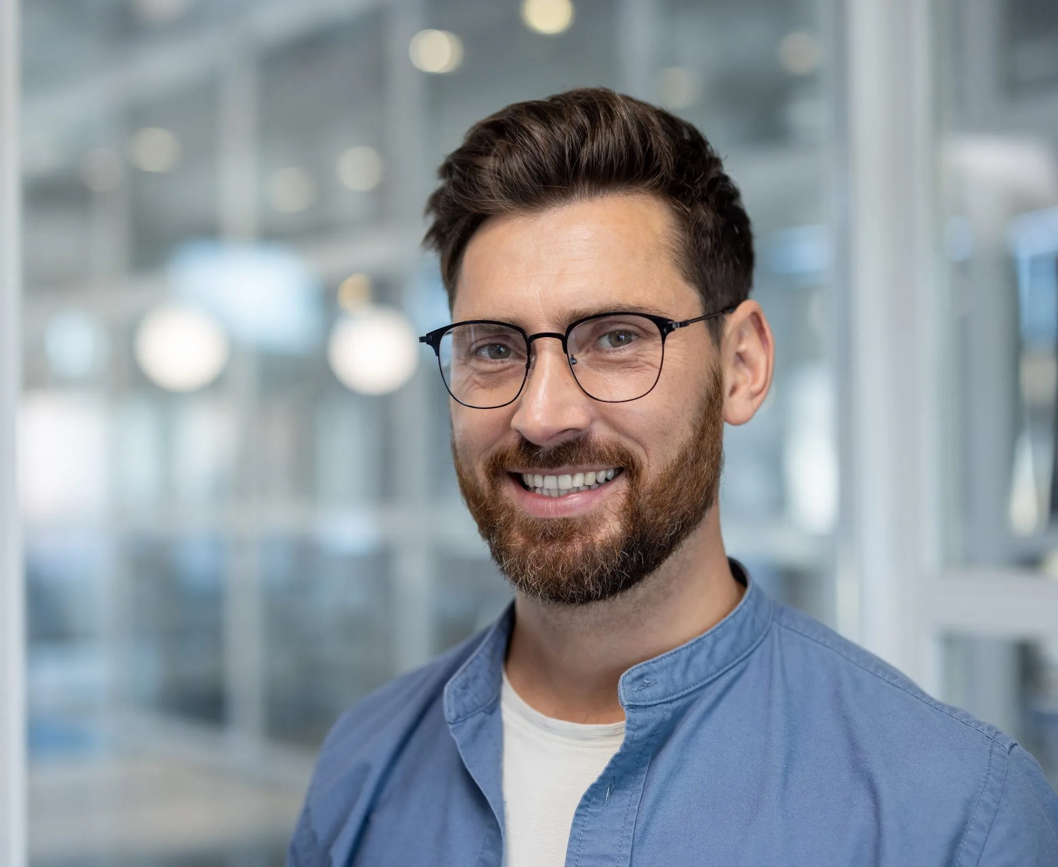 Smiling man wearing glasses and a blue shirt in a modern office setting