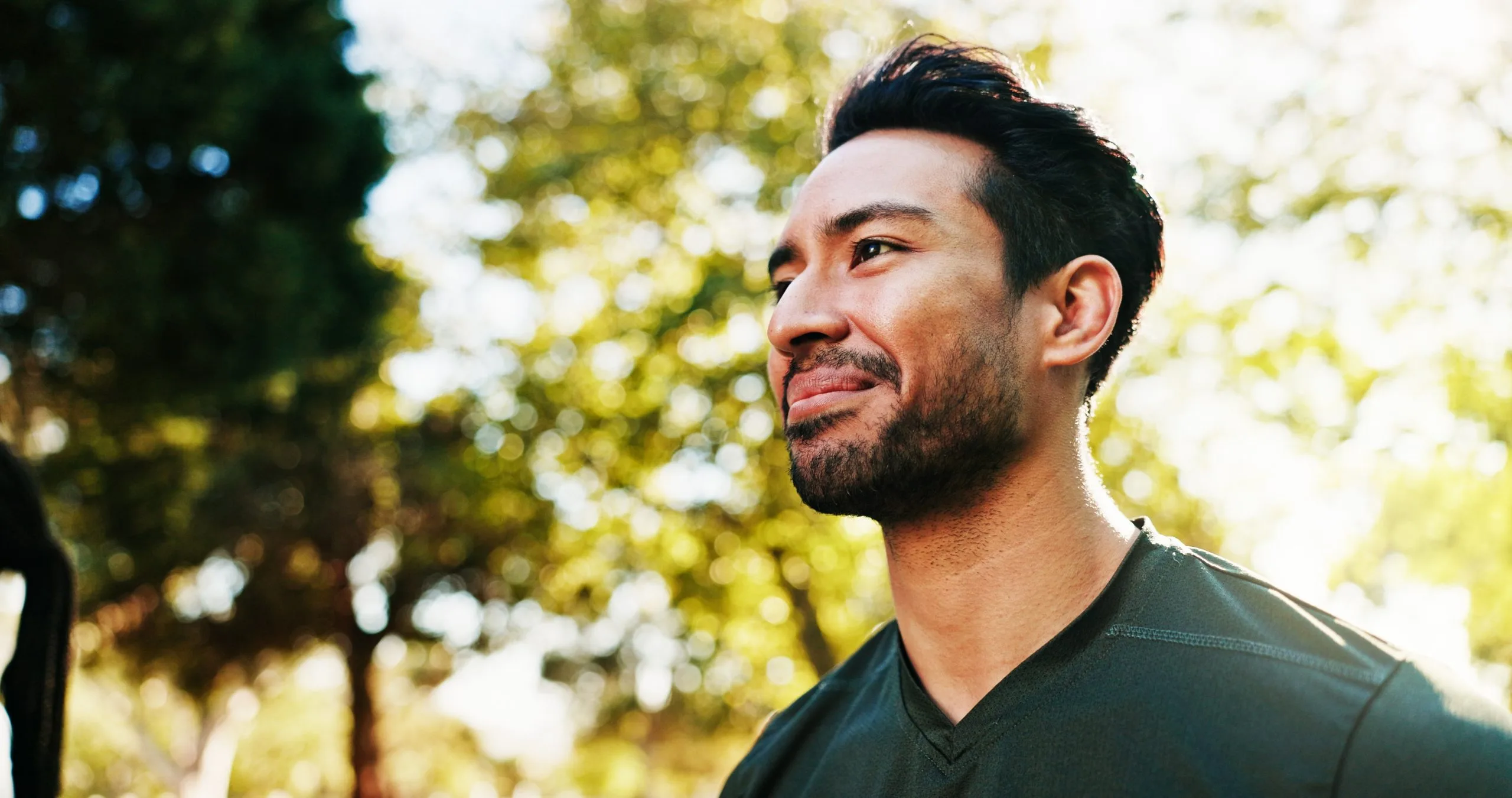 Man smiling outdoors surrounded by green foliage and dappled sunlight