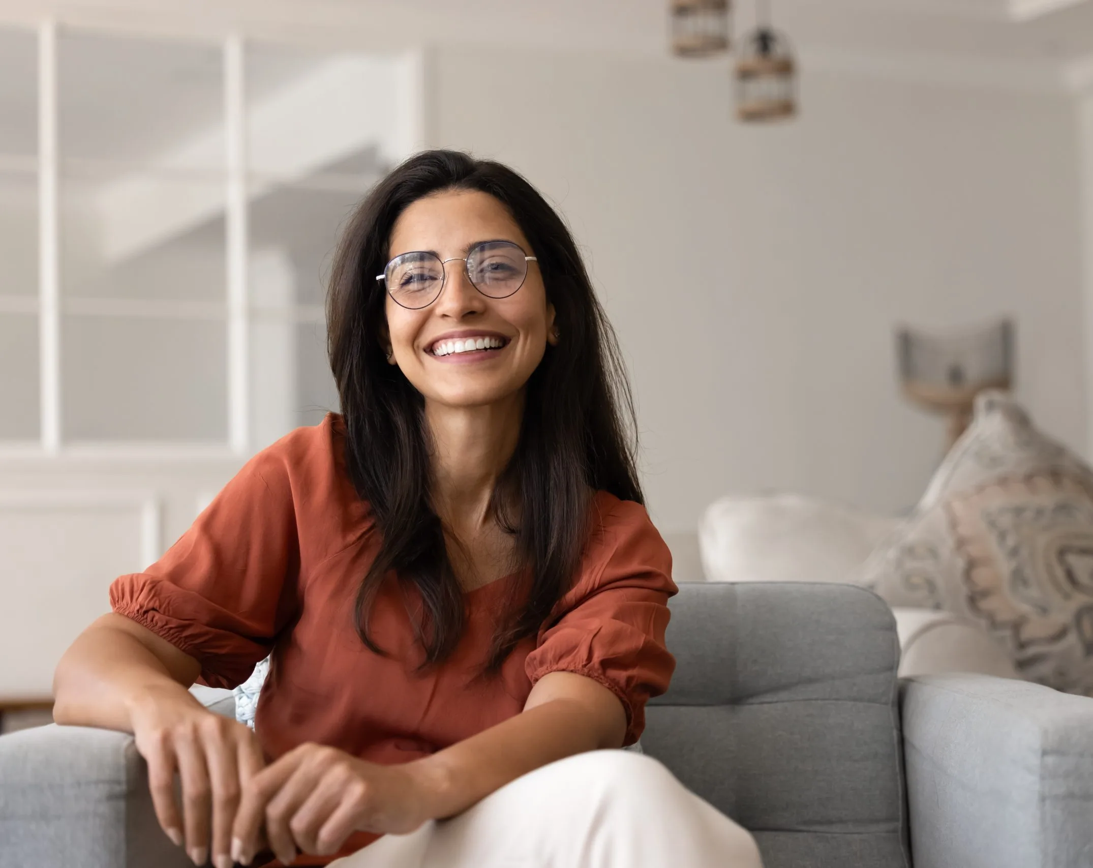 Woman wearing glasses smiling while sitting on a couch in a bright living room