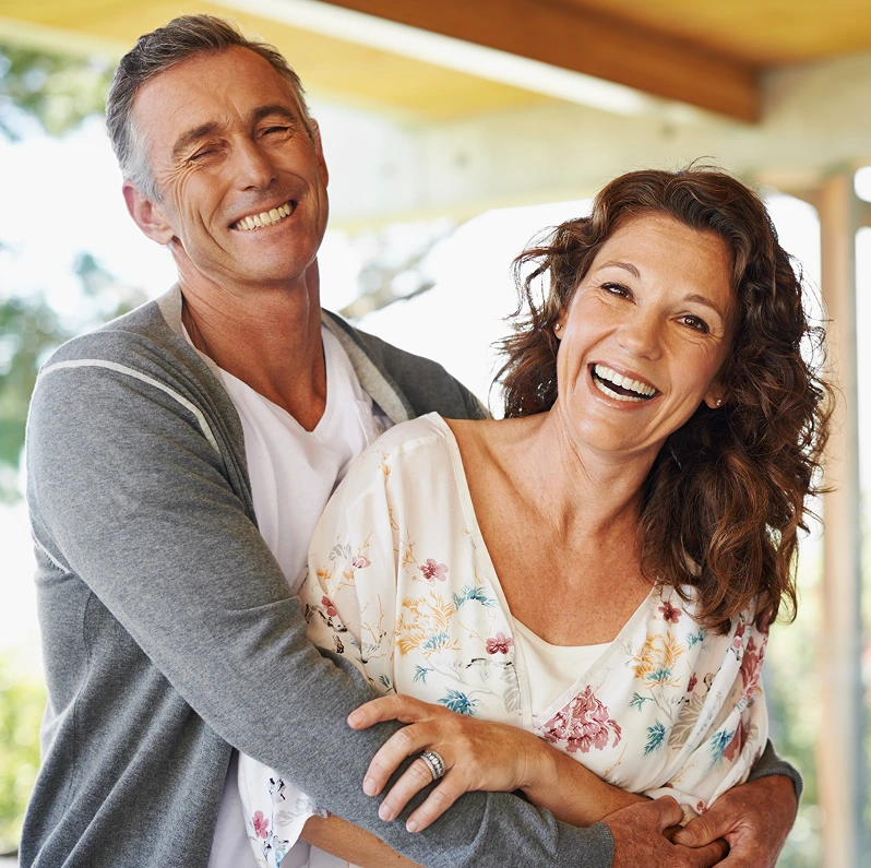 Middle-aged couple smiling together outdoors on a sunny porch