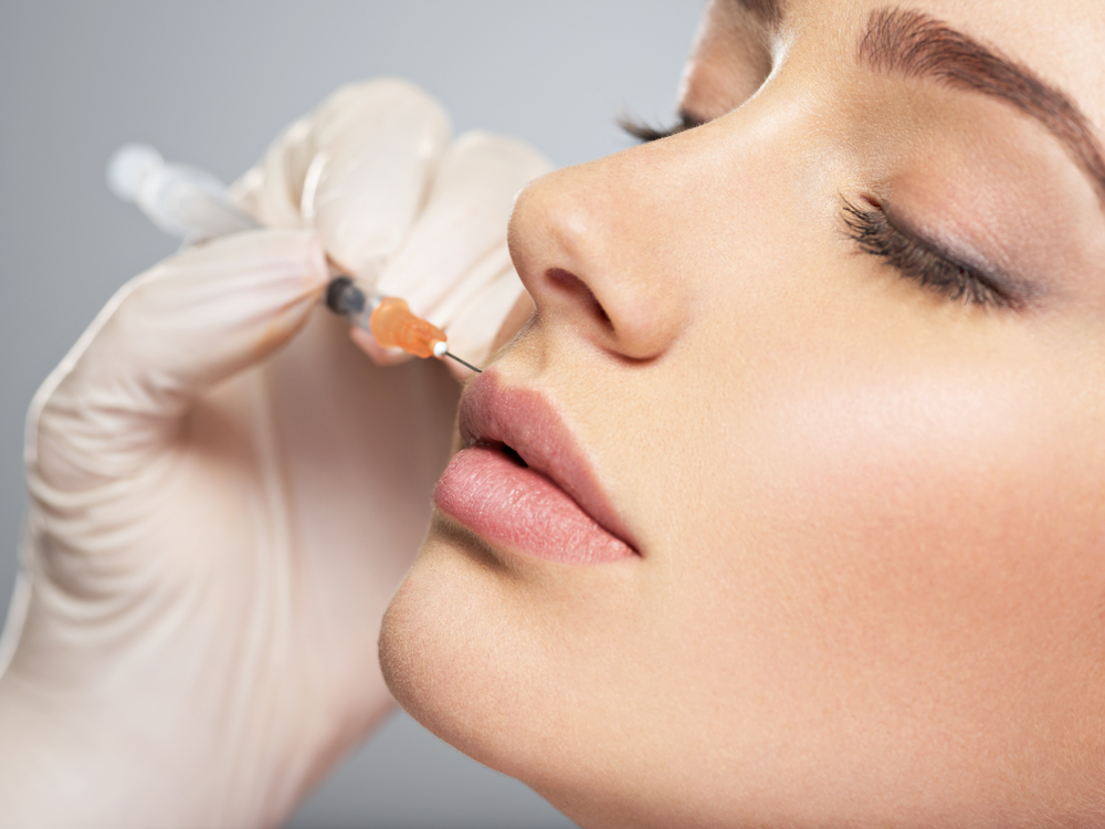 Practitioner injecting filler into patient's lips with syringe