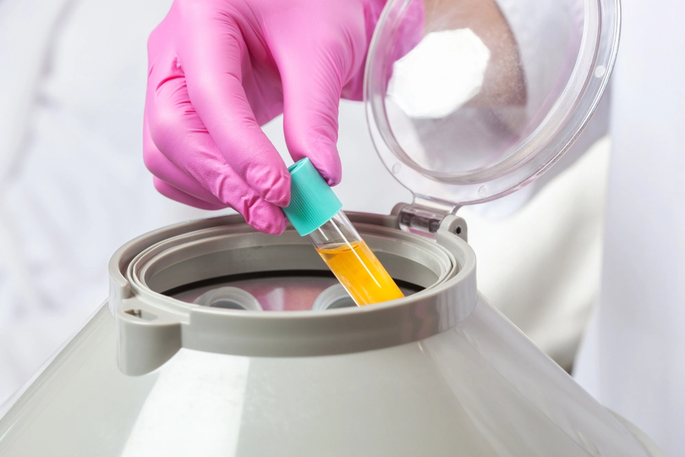 Gloved hand holding a dropper with yellow liquid over an open cosmetic treatment container