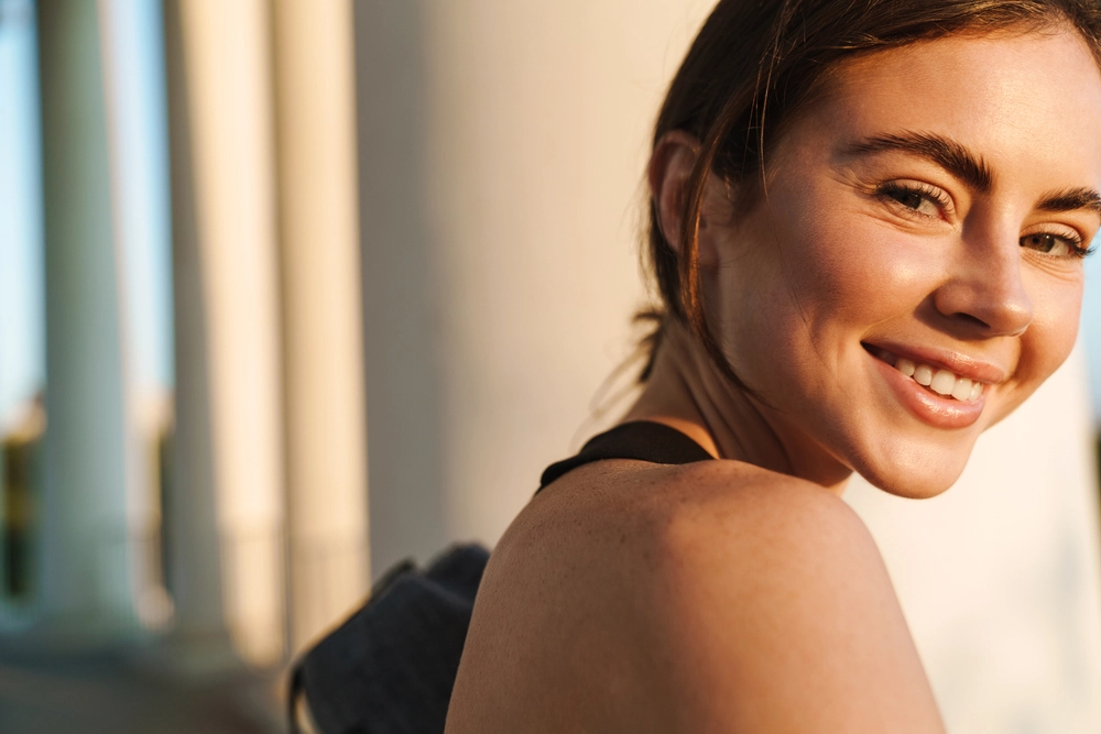 Woman smiling at camera over shoulder in natural sunlight
