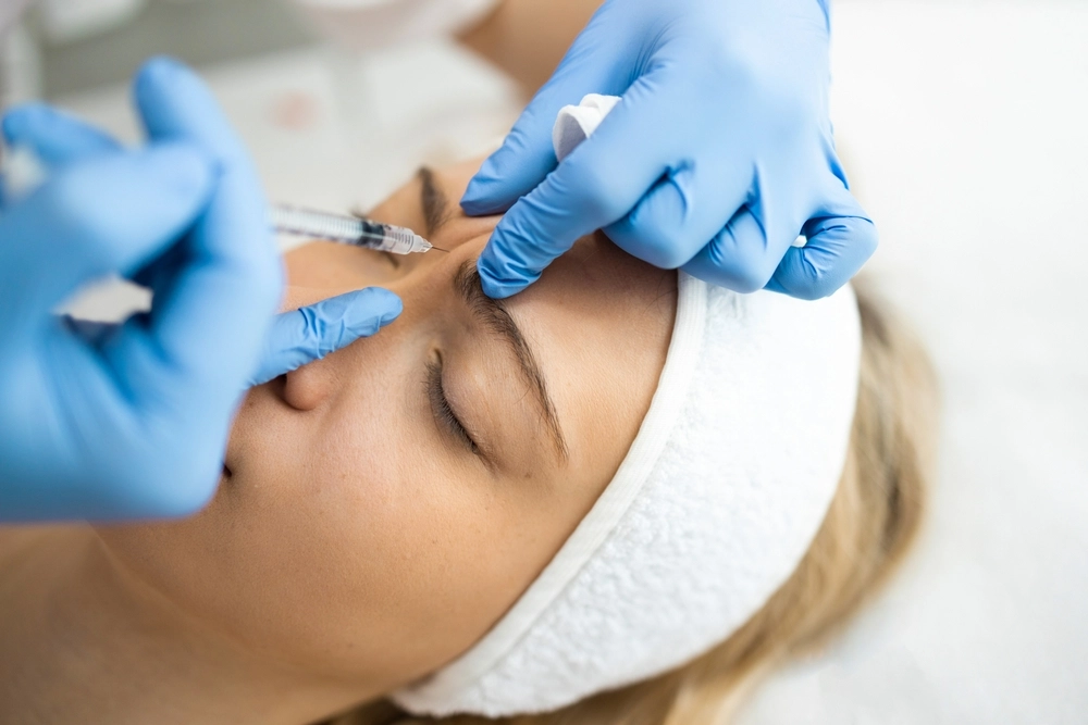 Practitioner injecting filler into patient's cheek area with syringe