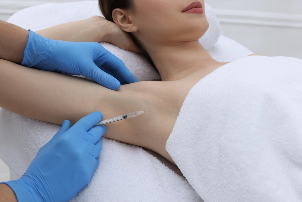 Practitioner in blue gloves injecting treatment into patient's underarm while patient reclines