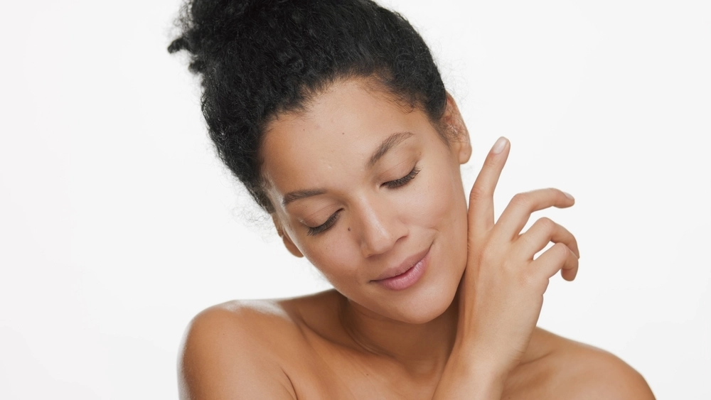 Woman with dark skin and closed eyes touching her neck and shoulder with a calm expression