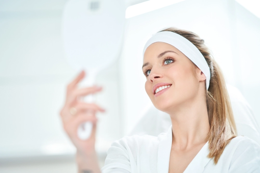 Patient with headband smiling while looking at mirror after aesthetic treatment