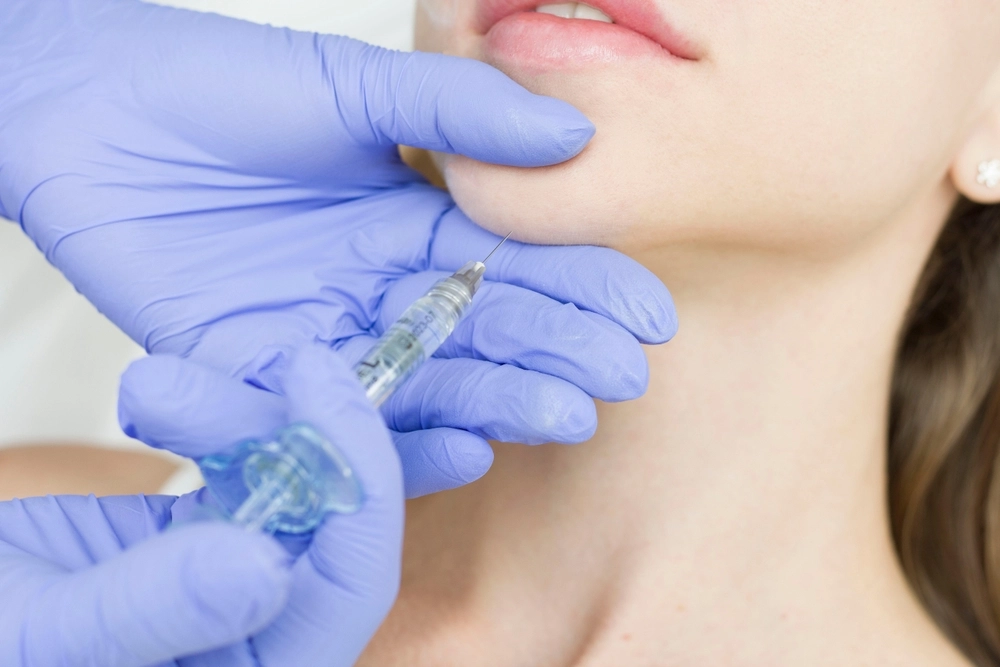 Provider in blue gloves preparing injectable treatment near patient's lips and jawline
