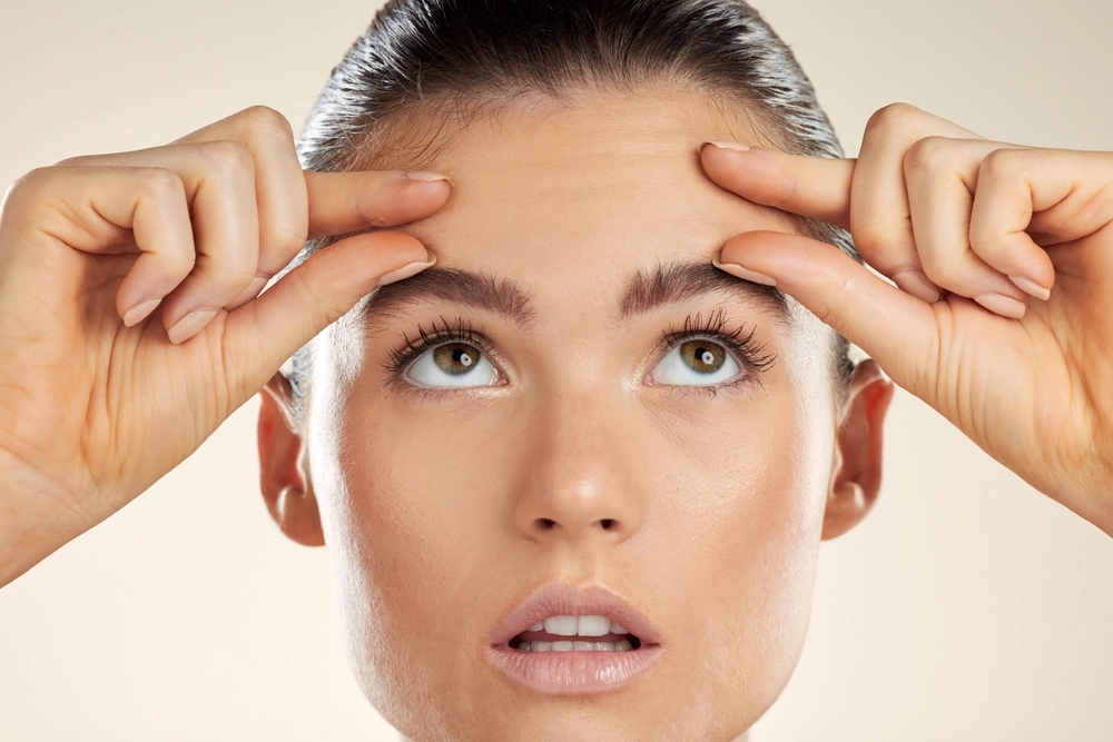 Woman pointing to forehead wrinkles with concerned expression