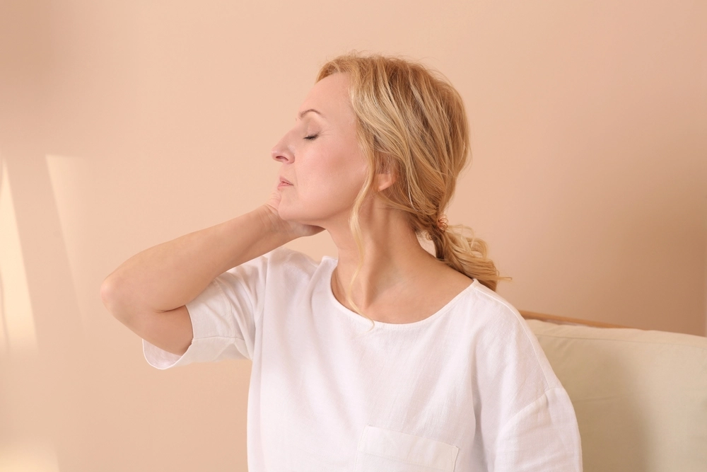 Woman in profile with hand on neck against neutral background