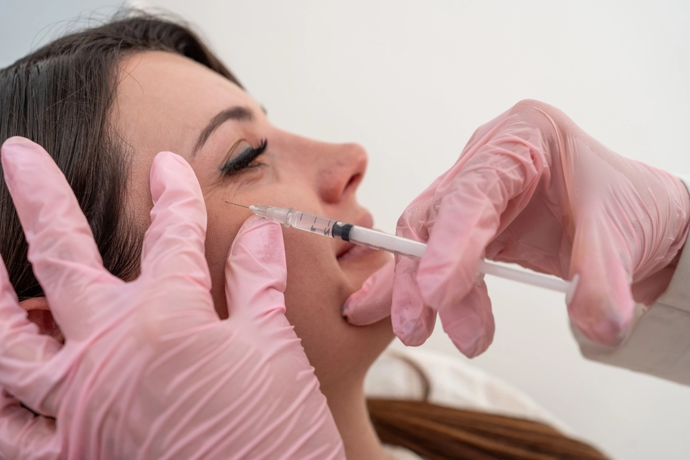 Practitioner in pink gloves injecting filler into patient's lips