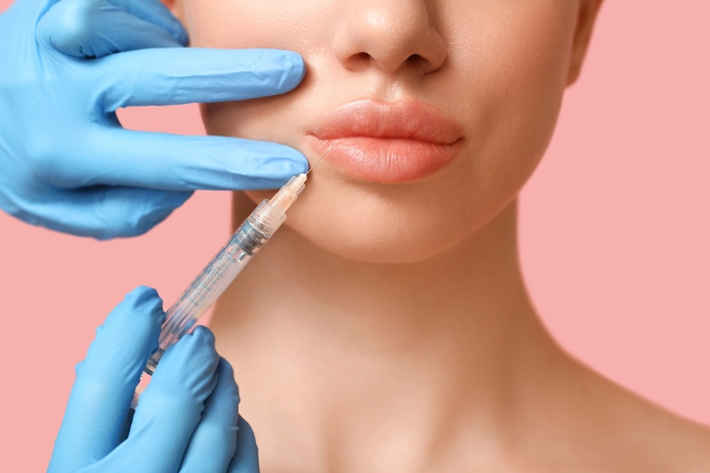 Practitioner in blue gloves holding syringe near patient's lips for injectable treatment