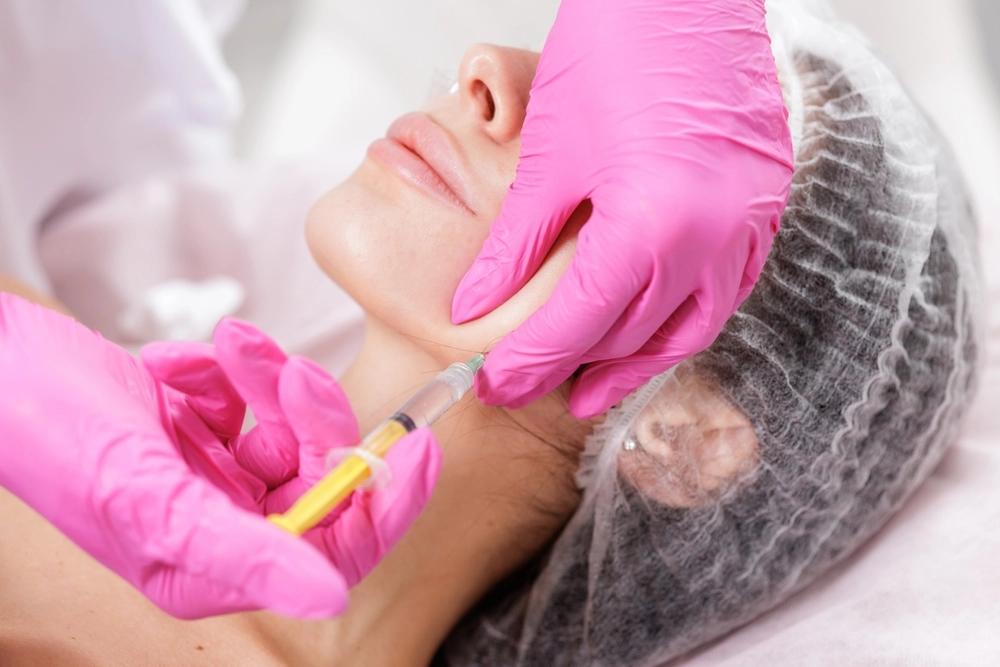 Provider wearing pink gloves administering an injection to patient's cheek during aesthetic treatment
