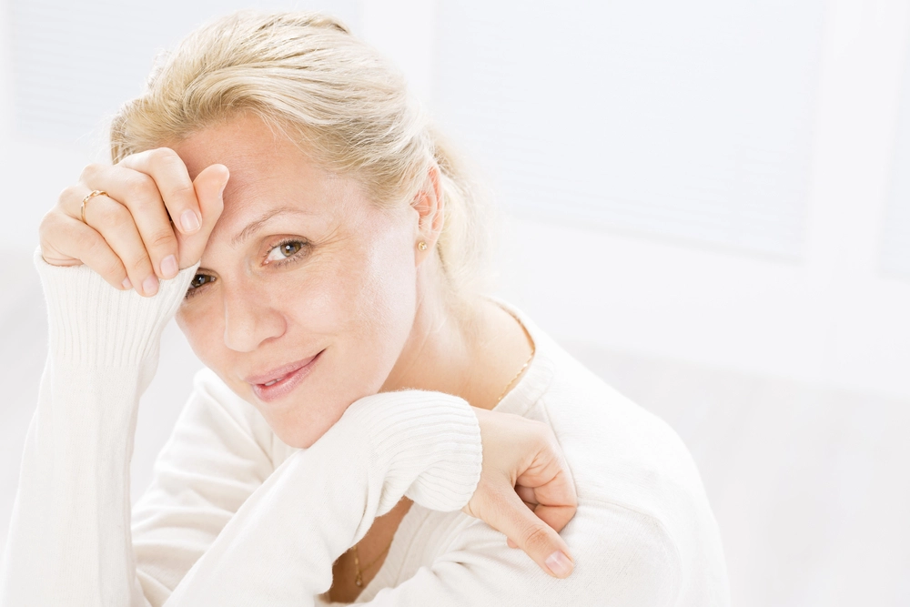 Blonde woman touching forehead with concerned expression against white background