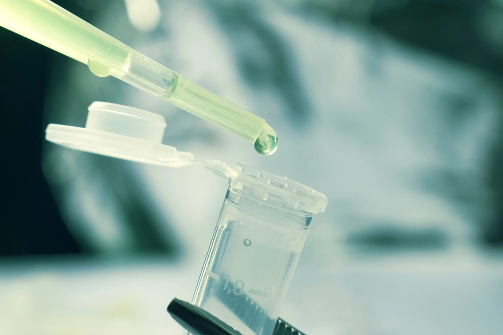Green liquid droplet falling from pipette into clear glass vial in clinical setting