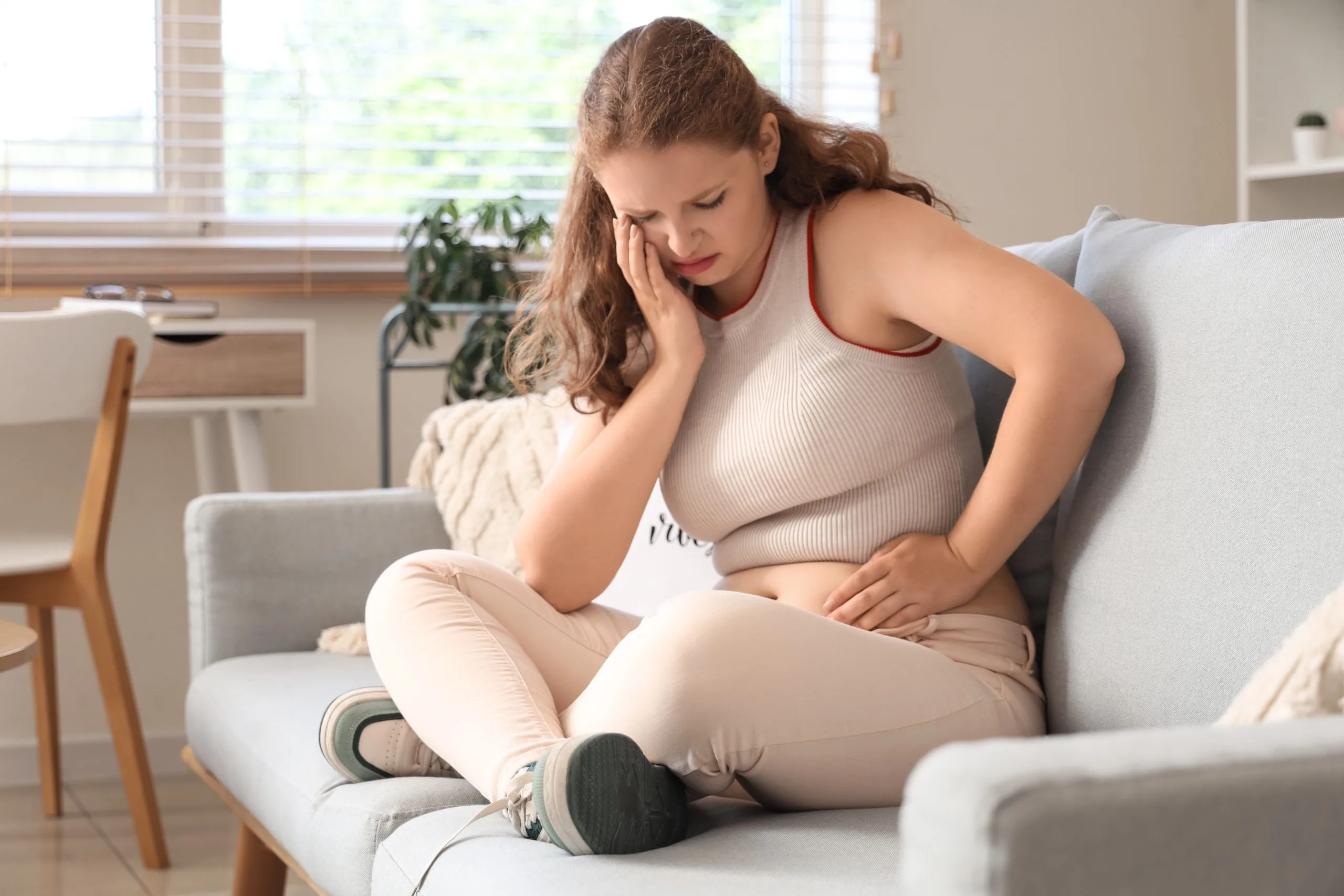 Woman sitting on a couch holding her stomach in discomfort