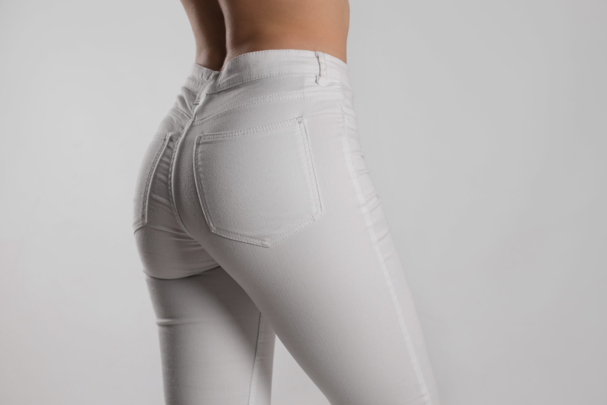 Woman wearing white jeans, rear view closeup against light background