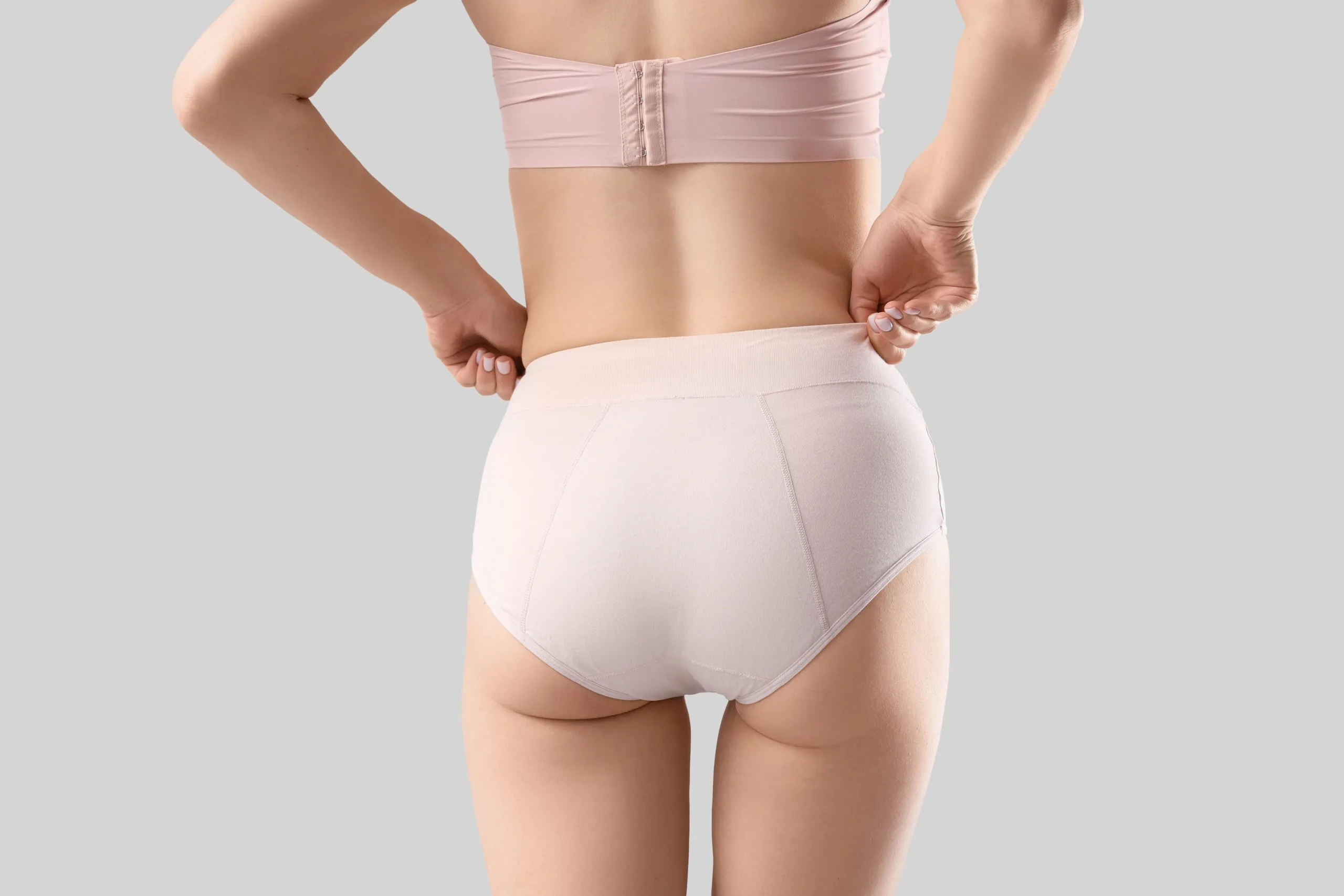 Woman from behind wearing beige undergarments, showing buttock contour