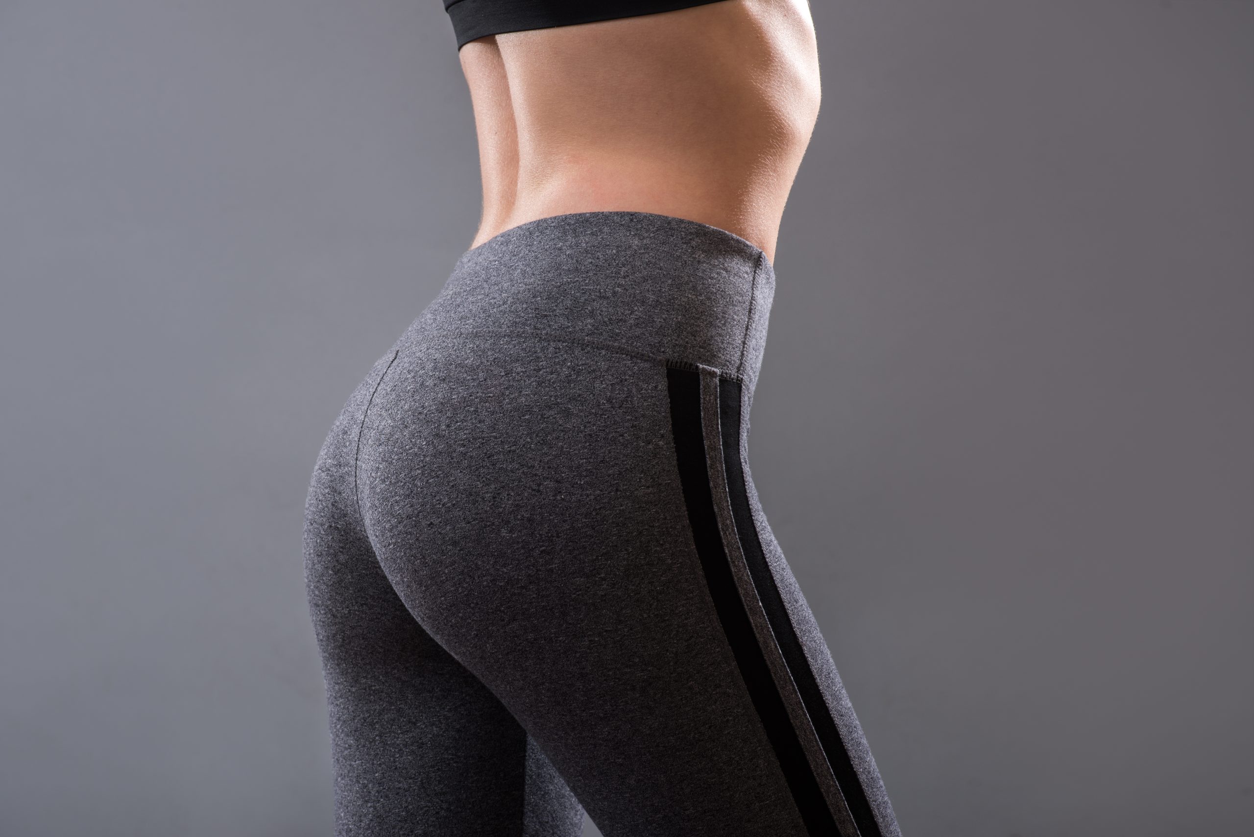 Woman wearing fitted gray leggings shown from the side against a neutral background